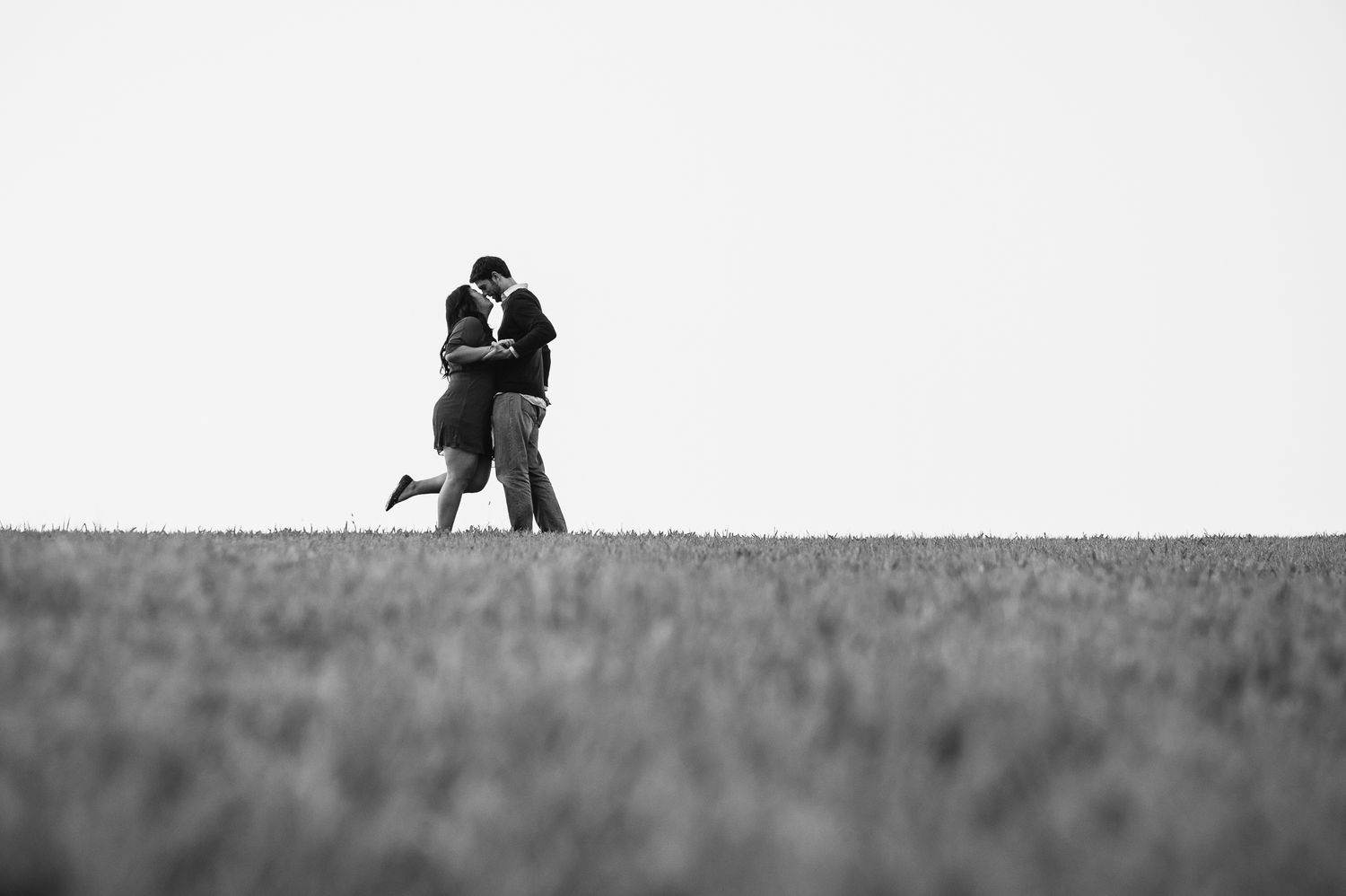 Black and white 35mm film silhouette of couple walking across field in Seoul, cinematic engagement photography with dramatic perspective