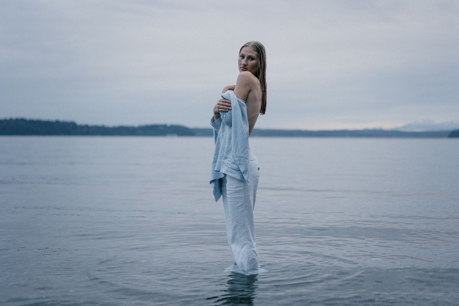 Seattle waterfront portrait with model in blue outfit standing in water, cinematic fashion photography with minimalist composition