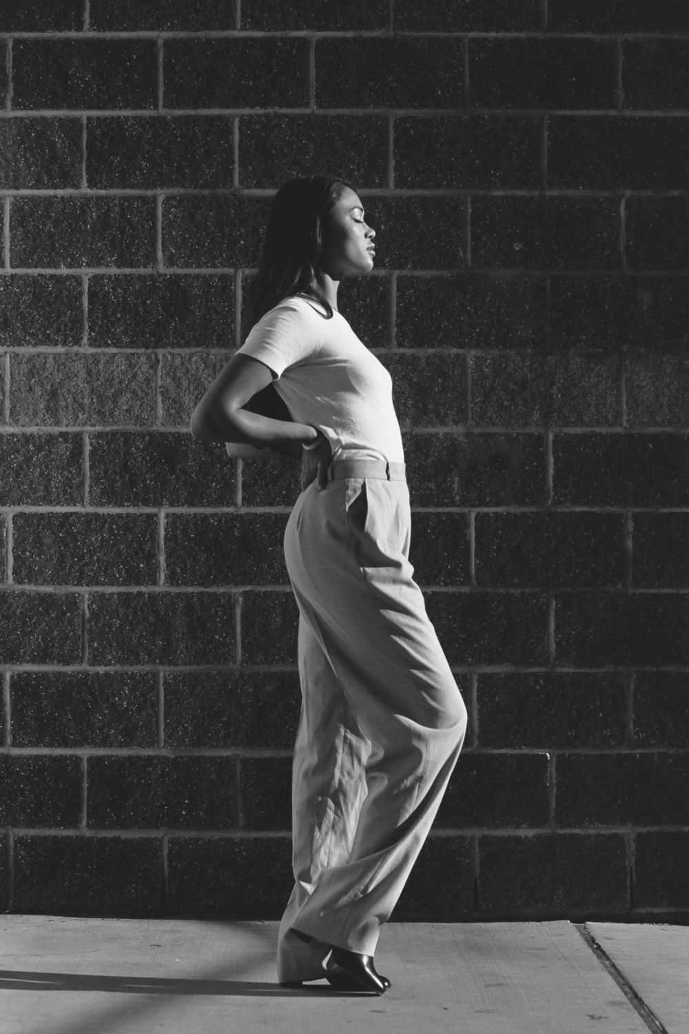 Black and white full-body portrait against brick wall, Seattle outdoor film photography with elegant pose and dramatic contrast