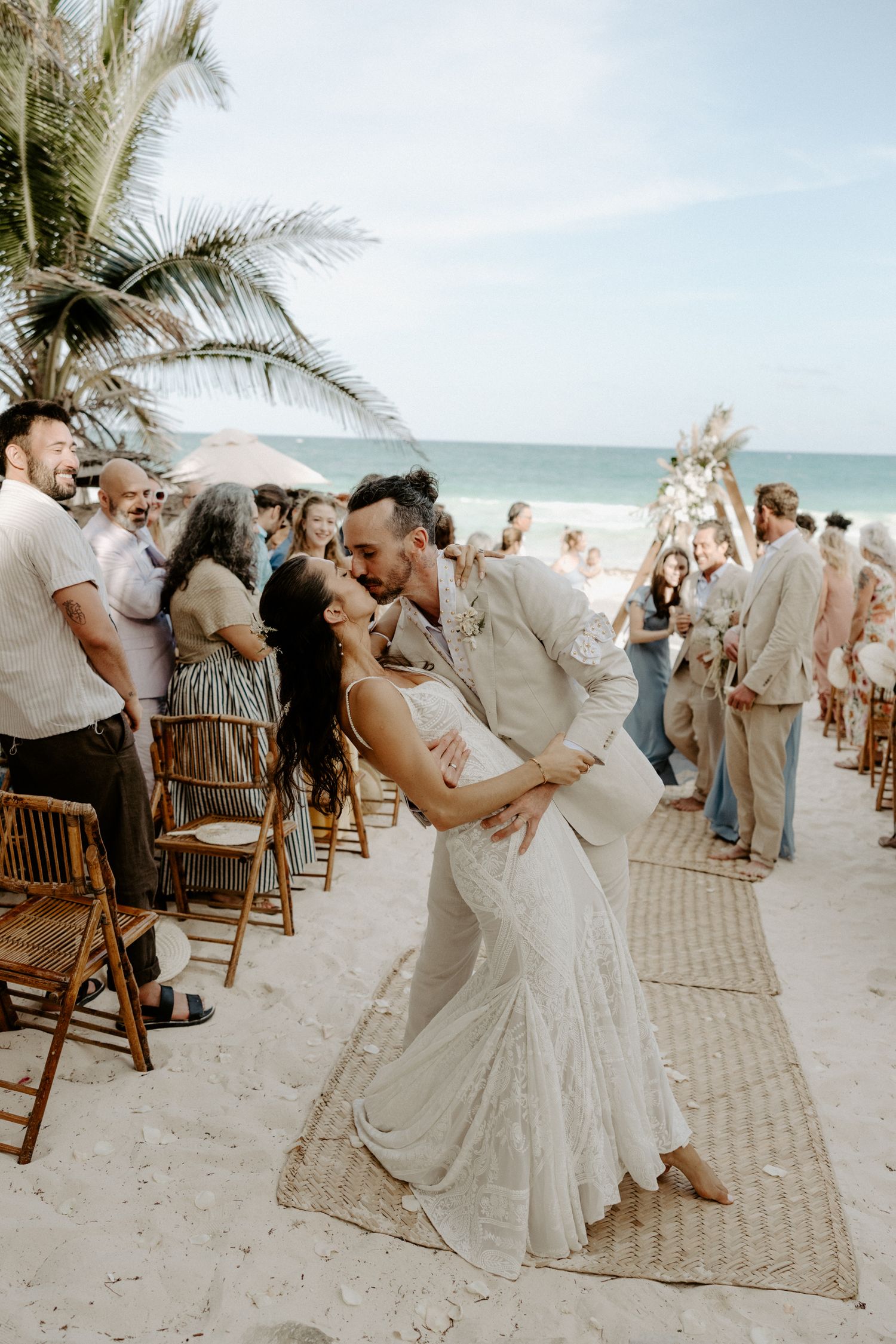 Bride and groom celebrating their destination wedding on Tulum's white sand beach surrounded by guests, palm trees and Mexican scenery