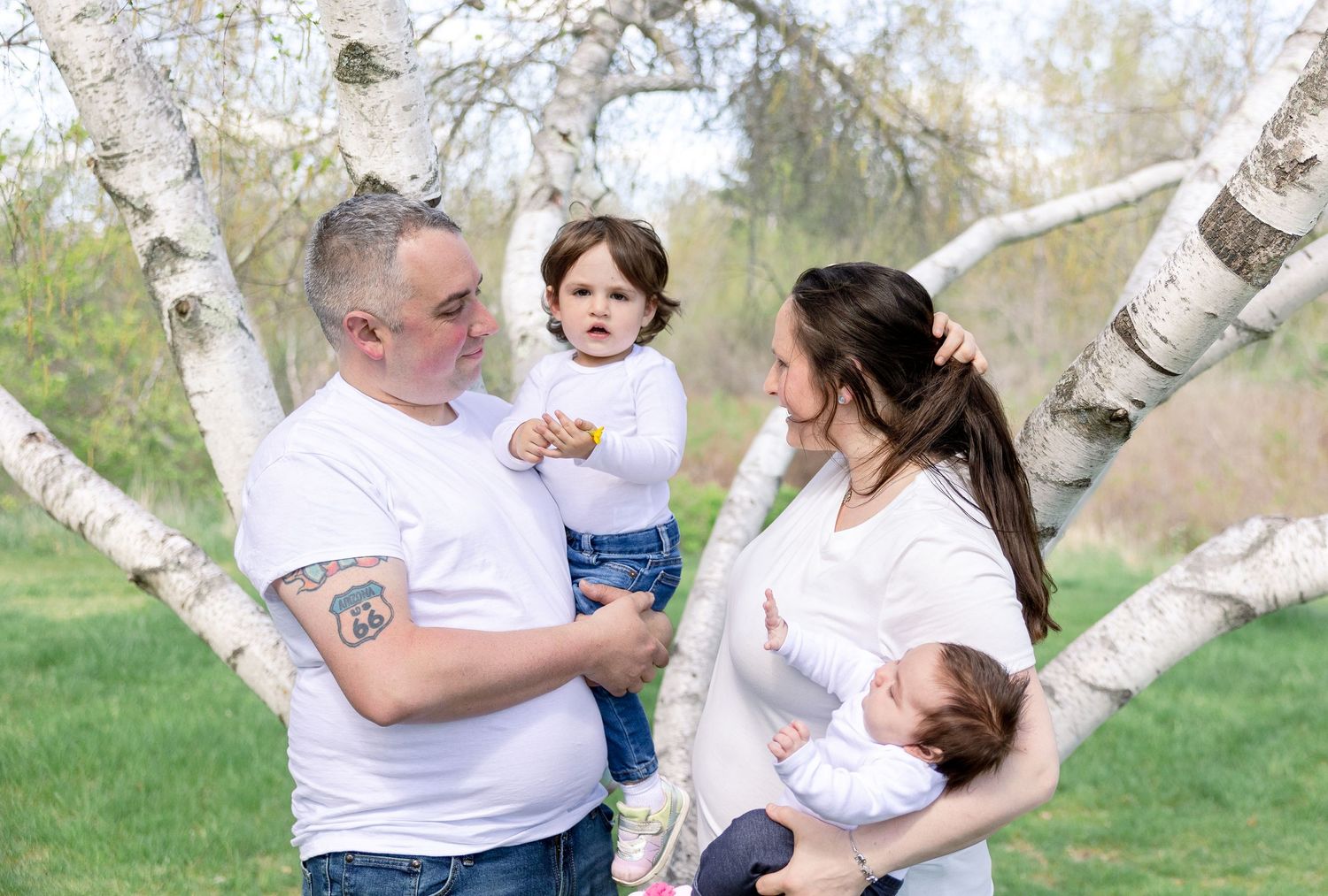 A family poses together outdoors among white birch trees on a grassy lawn.