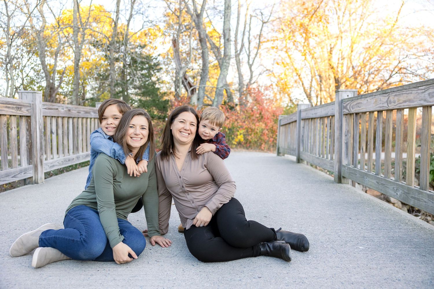 A group poses together on a wooden bridge path during autumn with colorful fall foliage in the background.