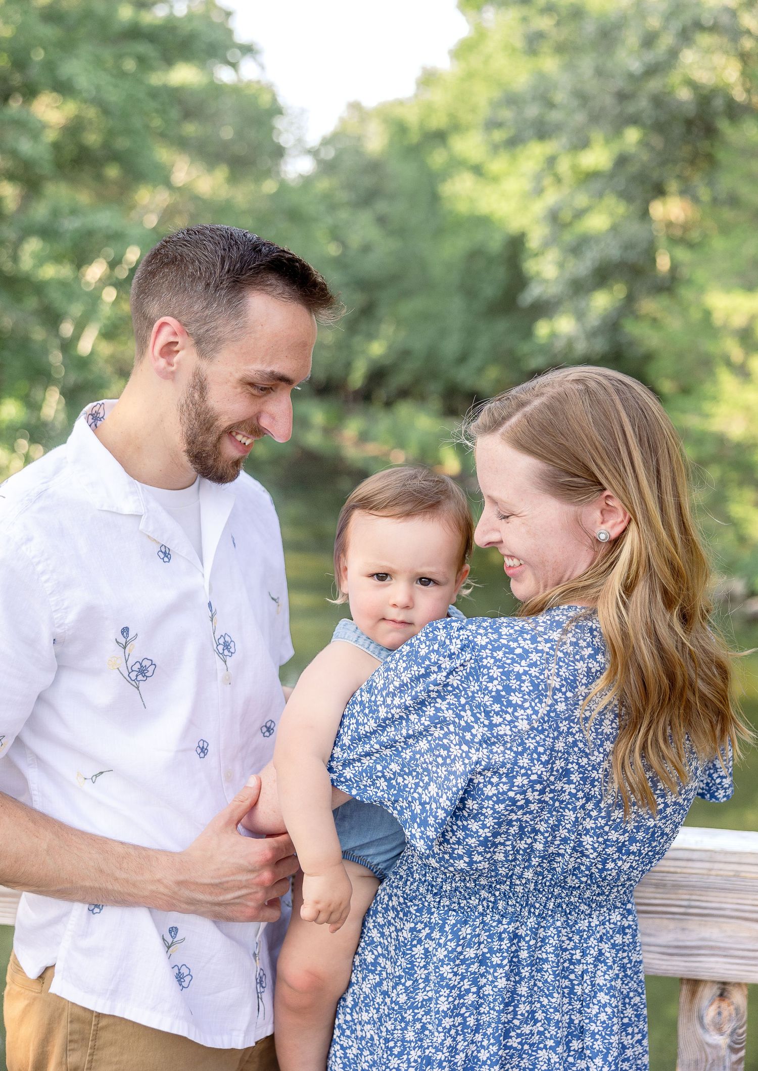 Parents sharing tender moment with baby outdoors in summer garden setting.