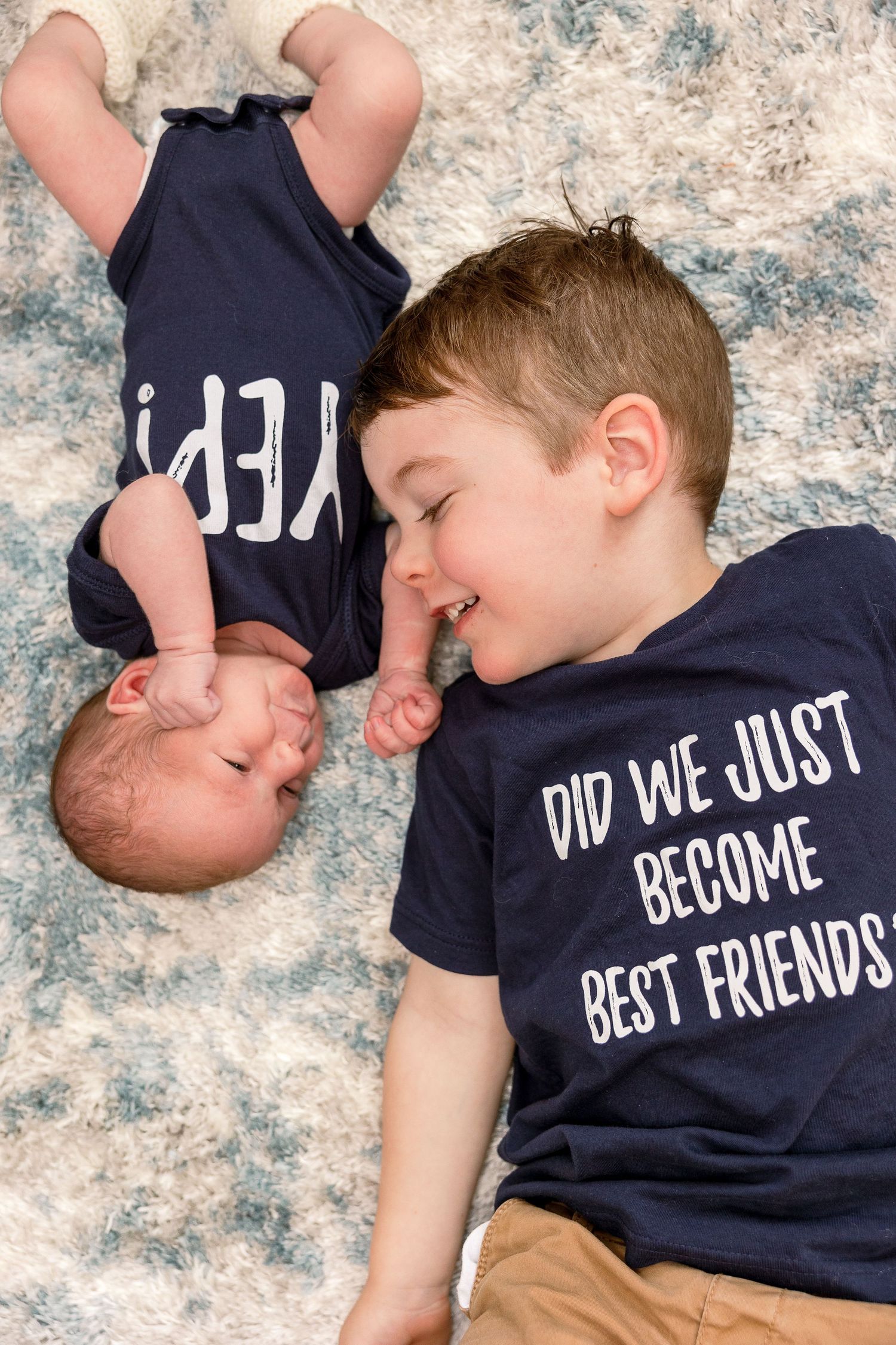Two children wearing matching navy t-shirts with text lying on a patterned rug together.