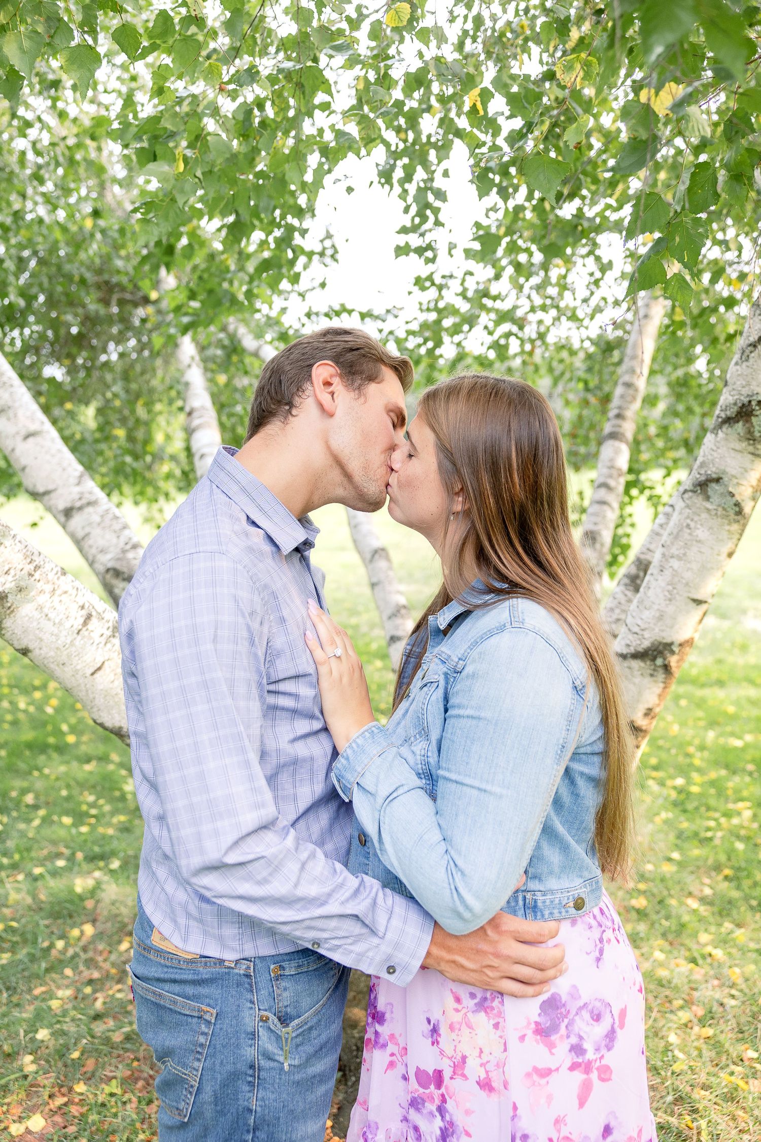 A romantic couple sharing a tender kiss in front of birch trees on a sunny spring day.