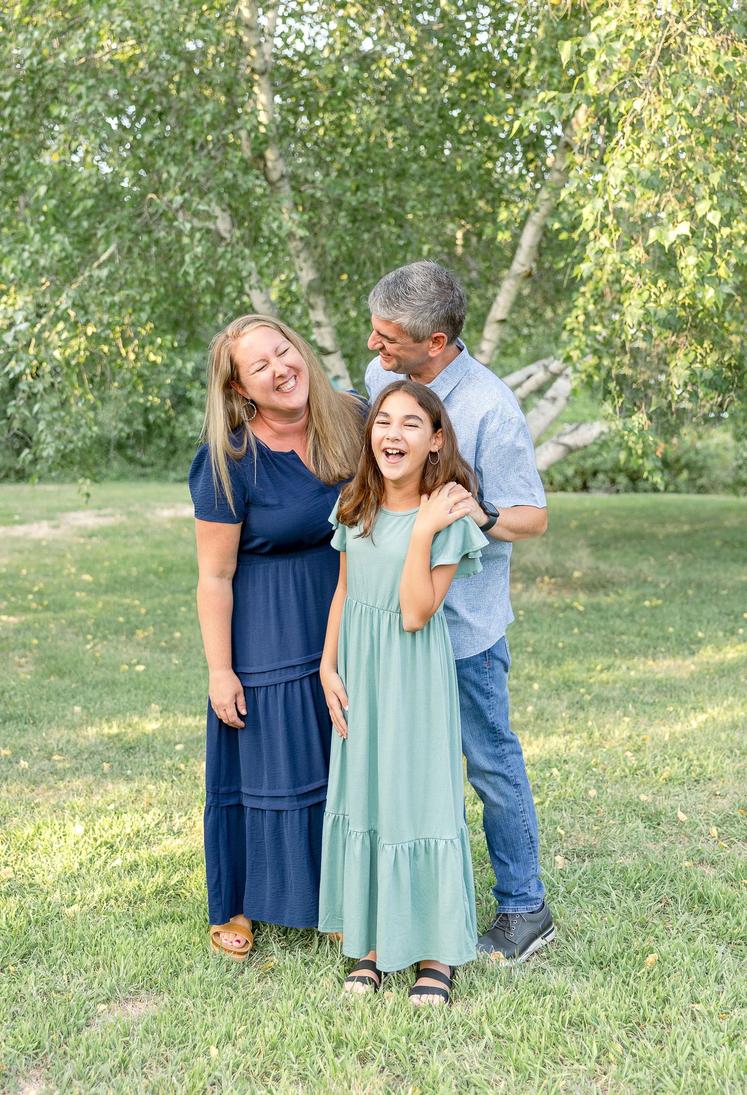A family shares joyful laughter while posing together in a park setting.