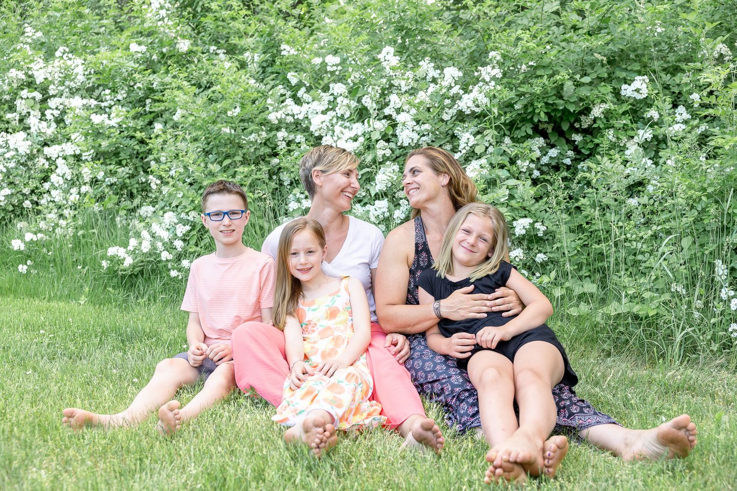 Family group sitting casually in lush green garden with white flowering bushes.