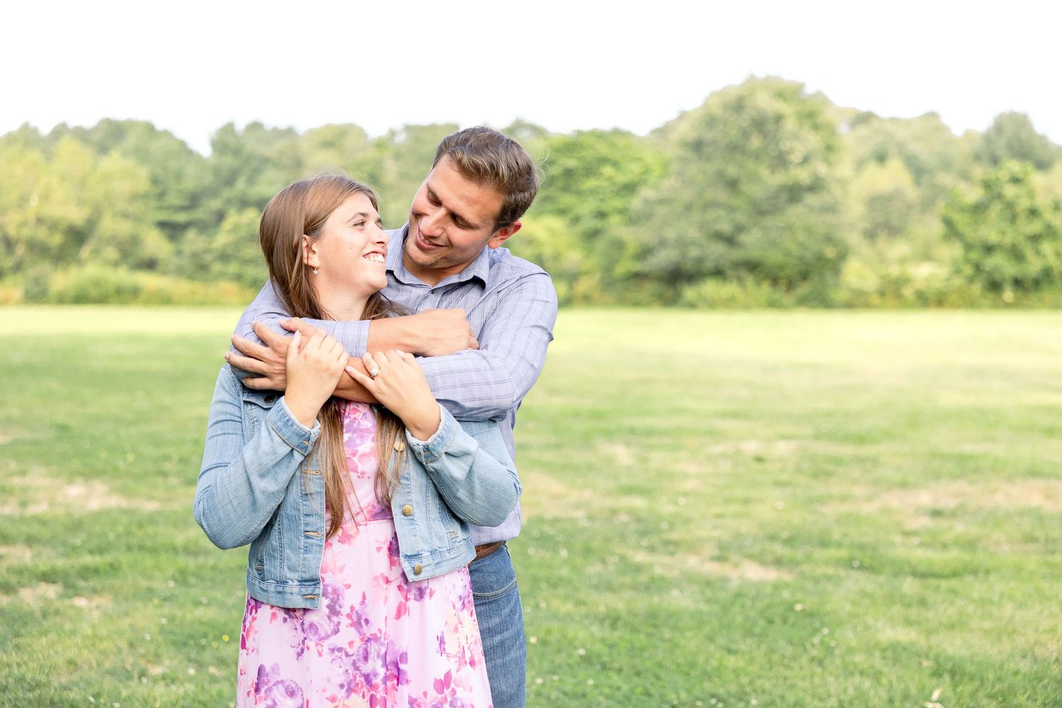 A couple embraces while sharing a joyful moment together in a sunny green meadow during springtime.