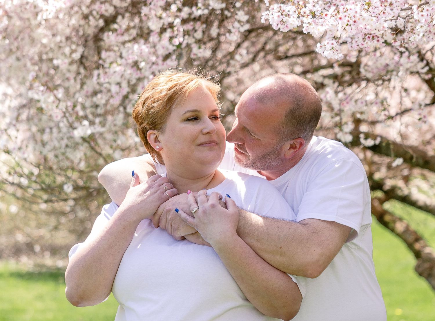 A couple embraces under blooming cherry blossom trees on a bright spring day.