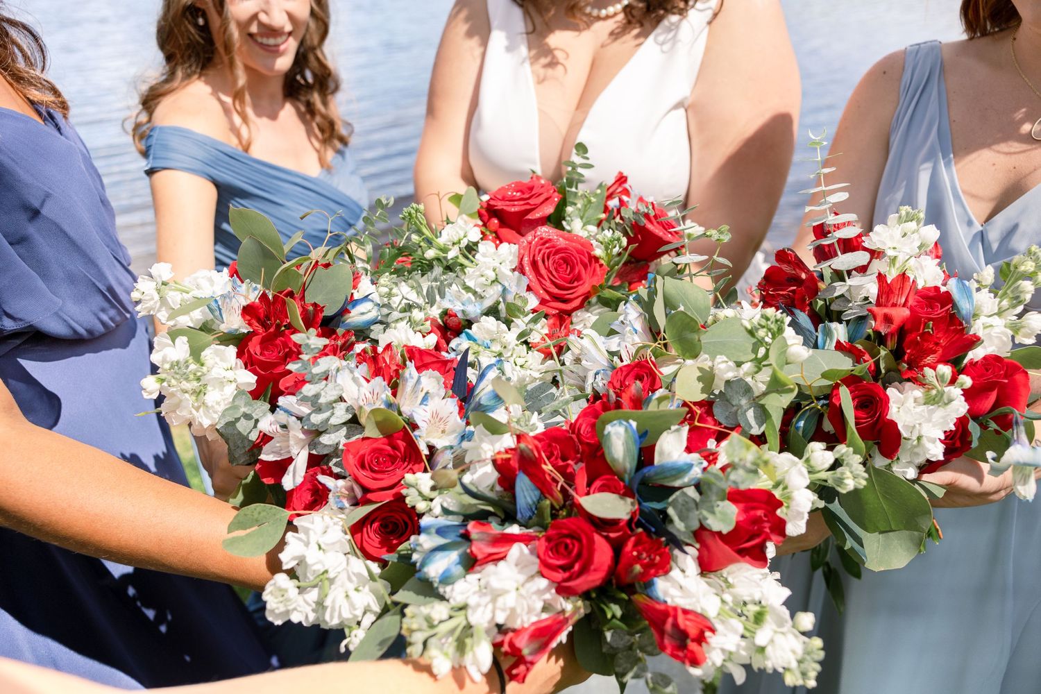 Wedding bouquets featuring red roses and white flowers with eucalyptus greenery held against light blue dresses.