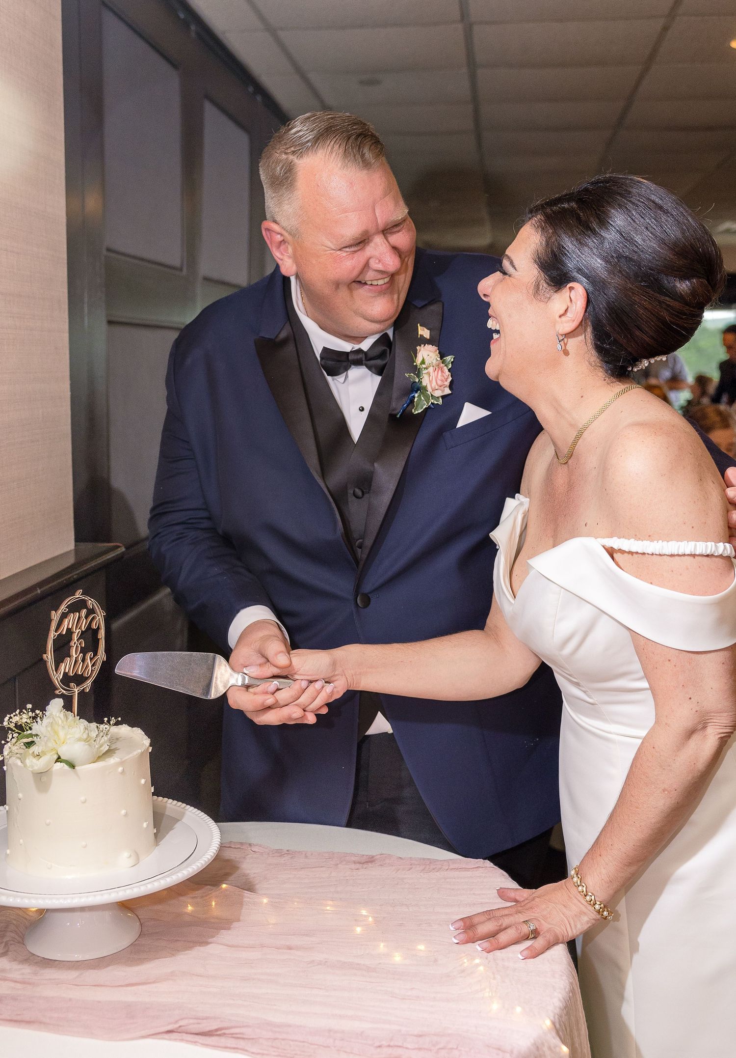 Newlyweds share a joyful moment while cutting their white wedding cake together at the reception.