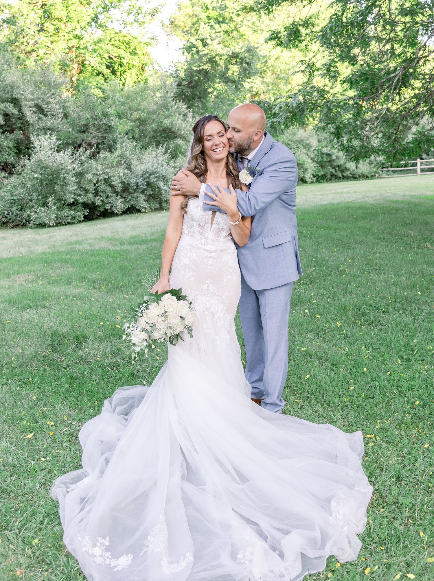 Joyful wedding couple embracing outdoors in formal attire with flowing white gown.