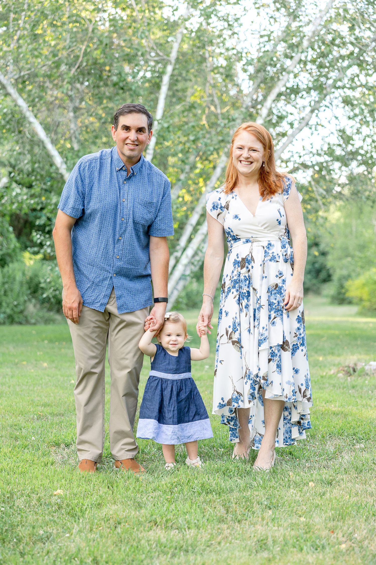 A family in coordinated blue outfits poses together on grass with birch trees in background.