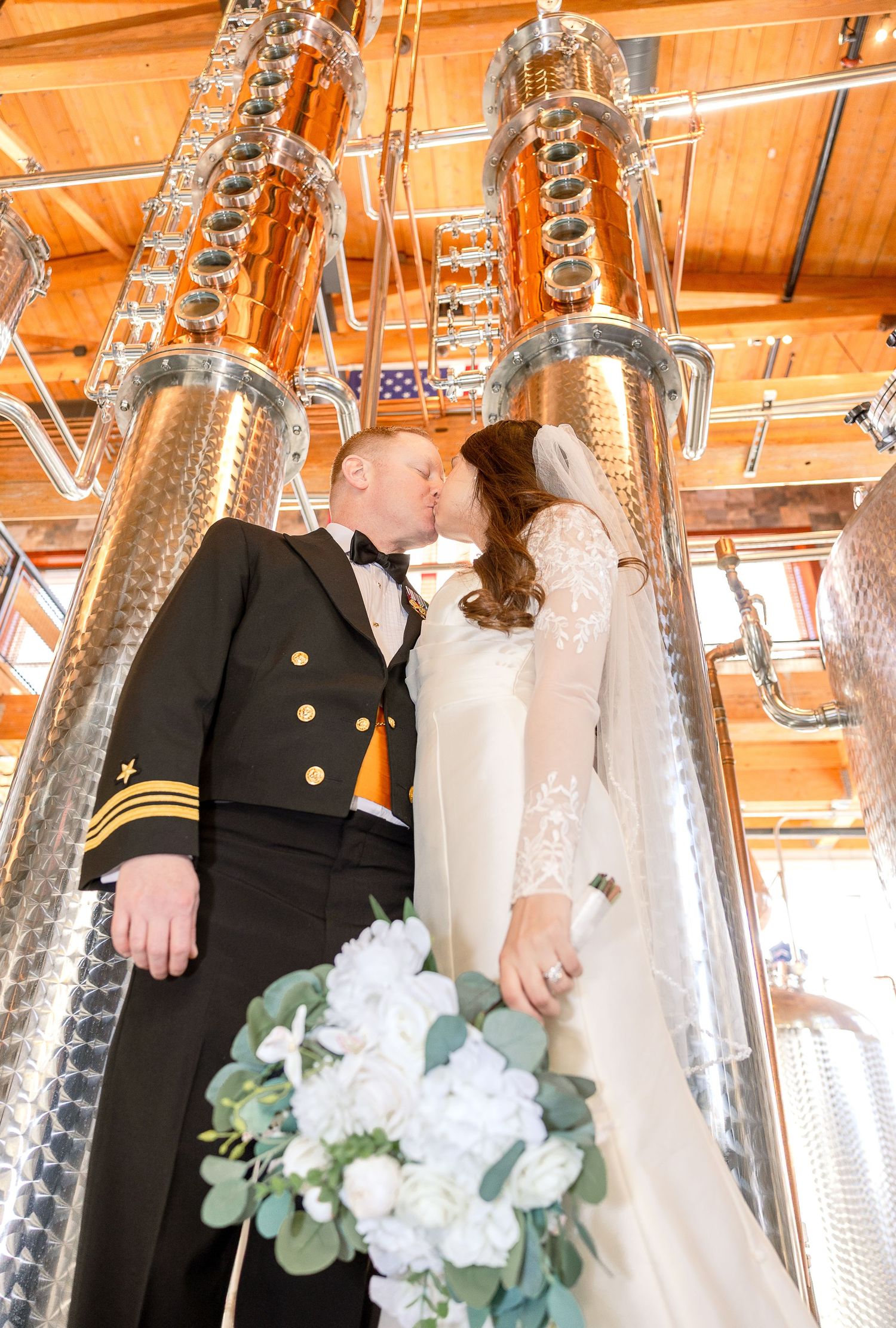 Wedding couple shares an intimate moment between large stainless steel distillery tanks with wood ceiling above.