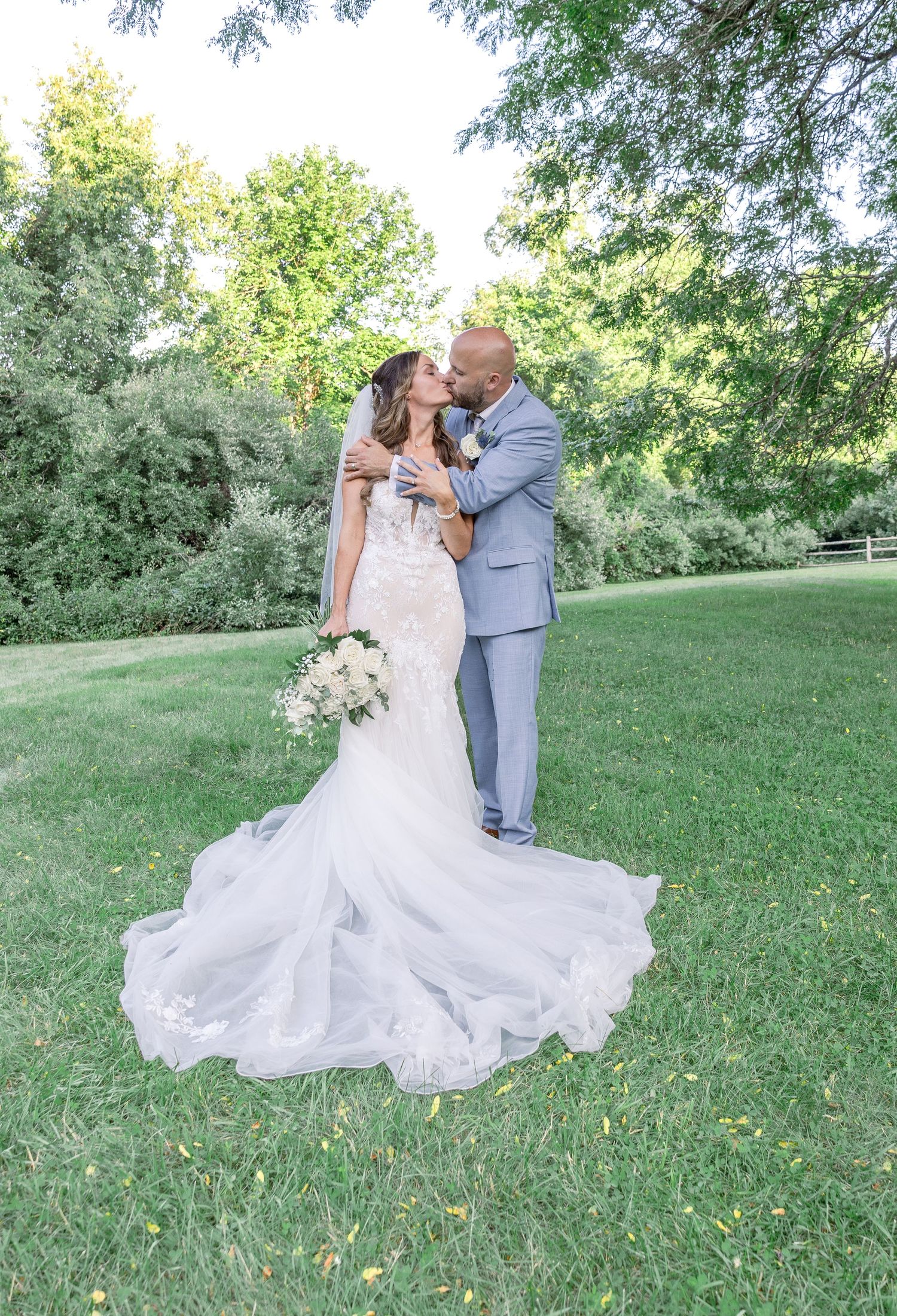 Couple in wedding attire sharing a romantic moment on lush green lawn with beautiful white flowing bridal gown.