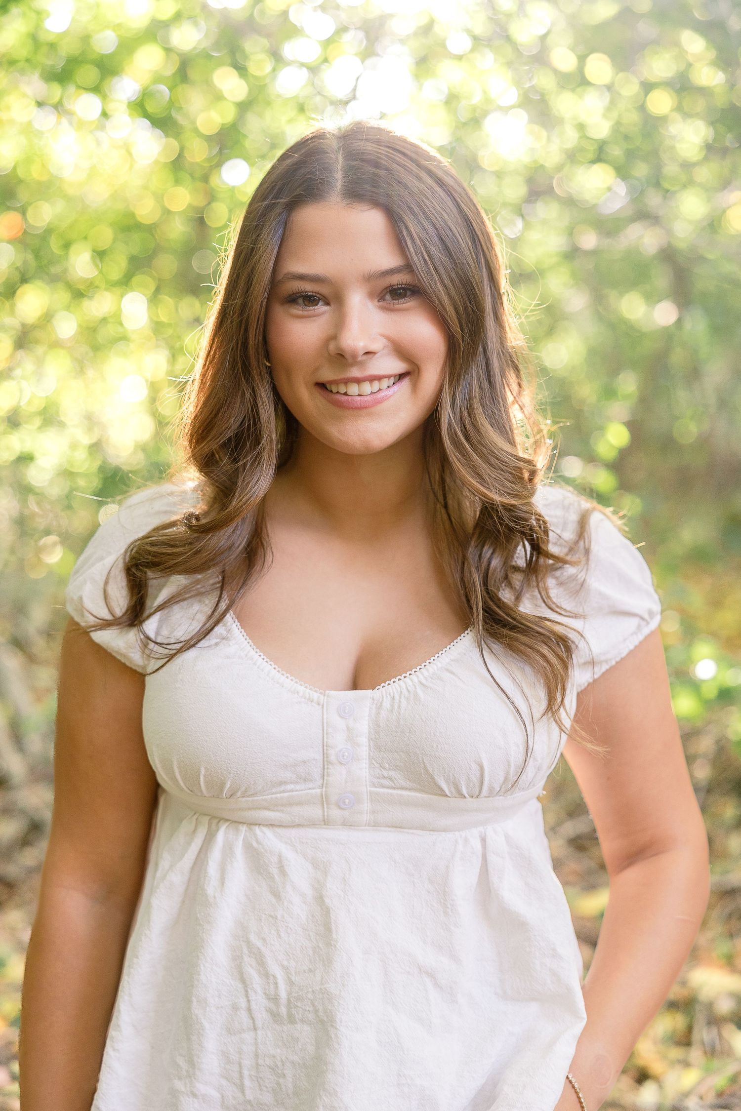 Beautiful outdoor portrait with natural bokeh lighting behind in a white summer dress with cap sleeves.