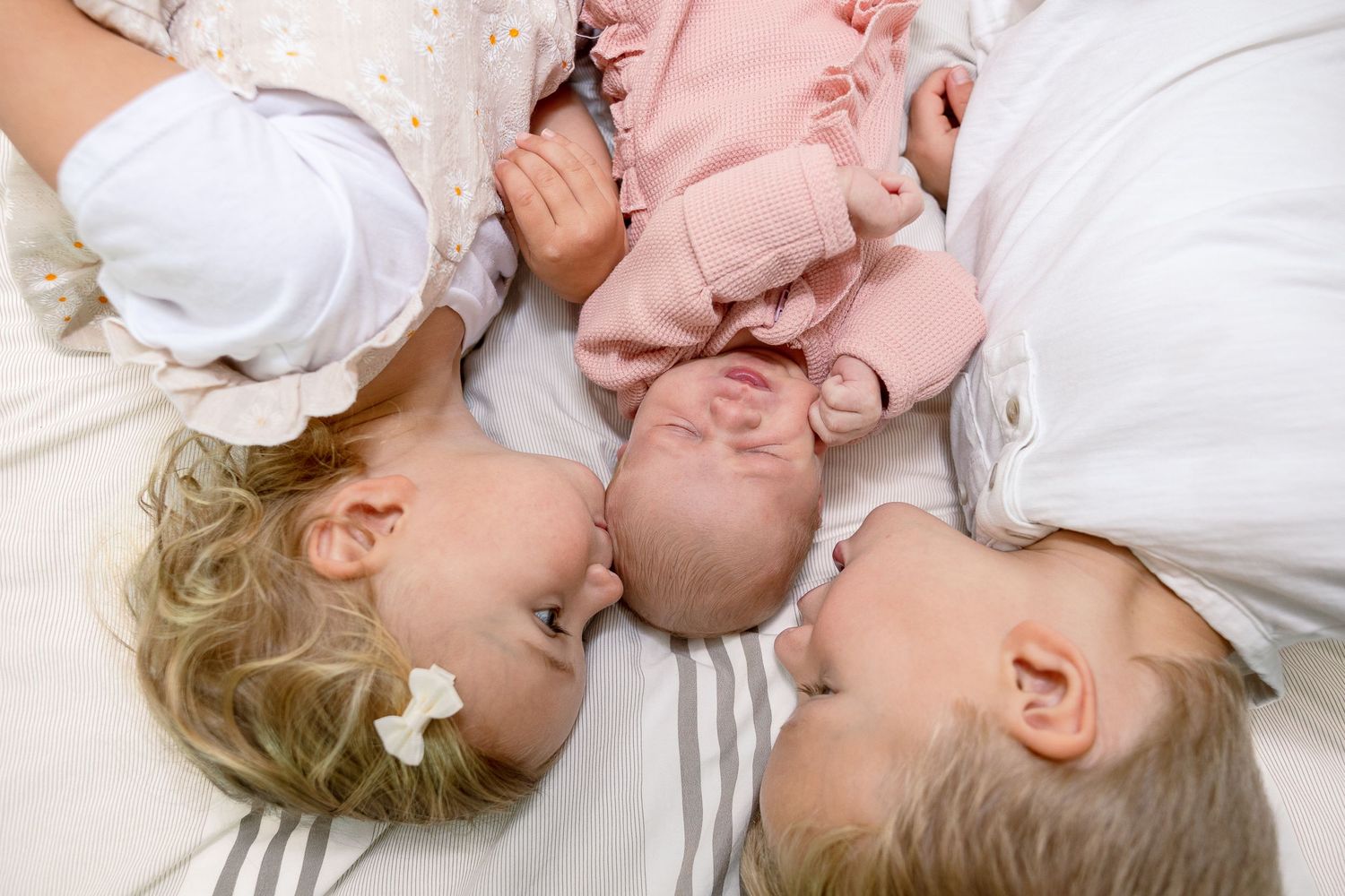 Three small children lying together on white bedding forming a circle.