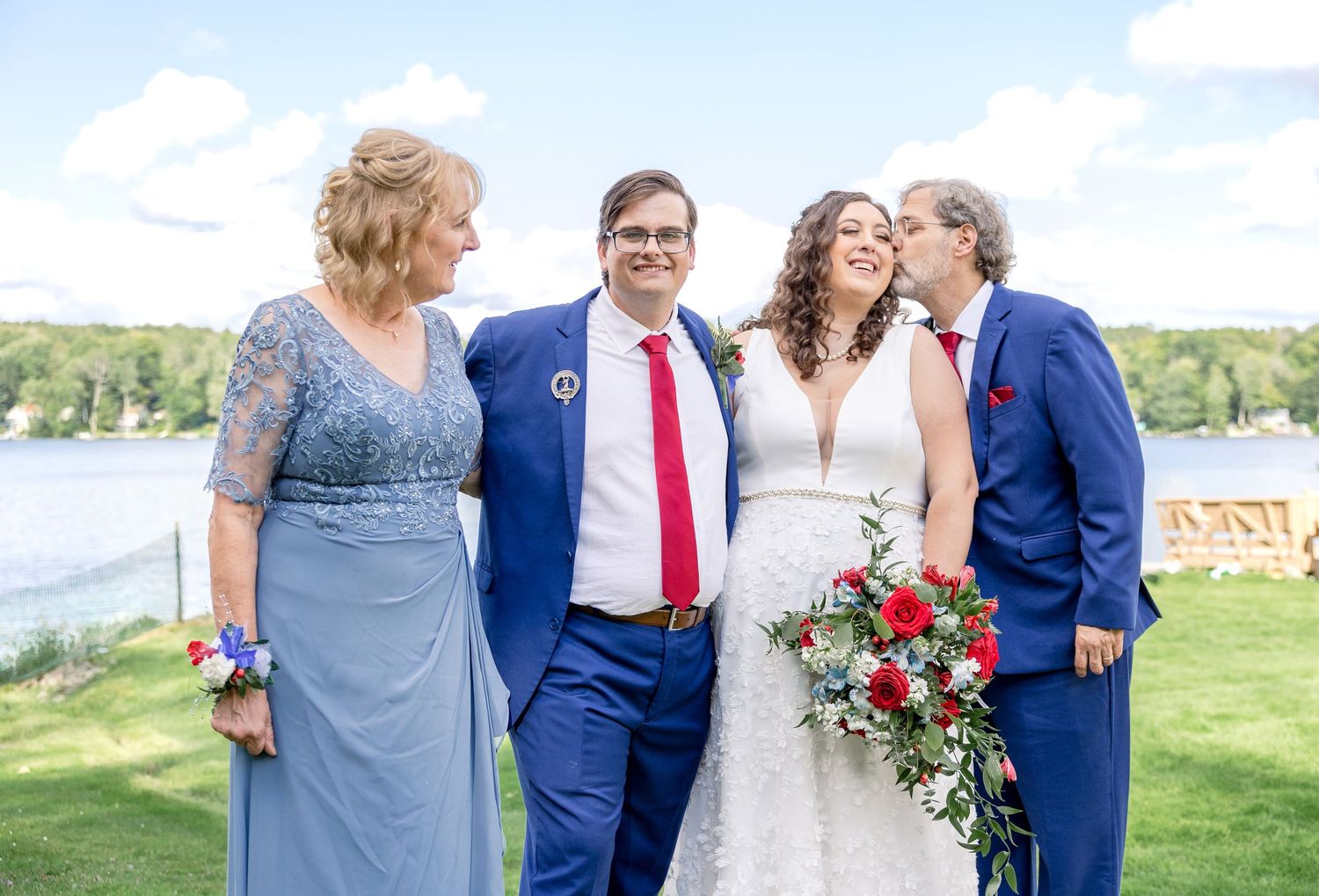 A group stands together outdoors by a lake during a wedding celebration on a sunny day.