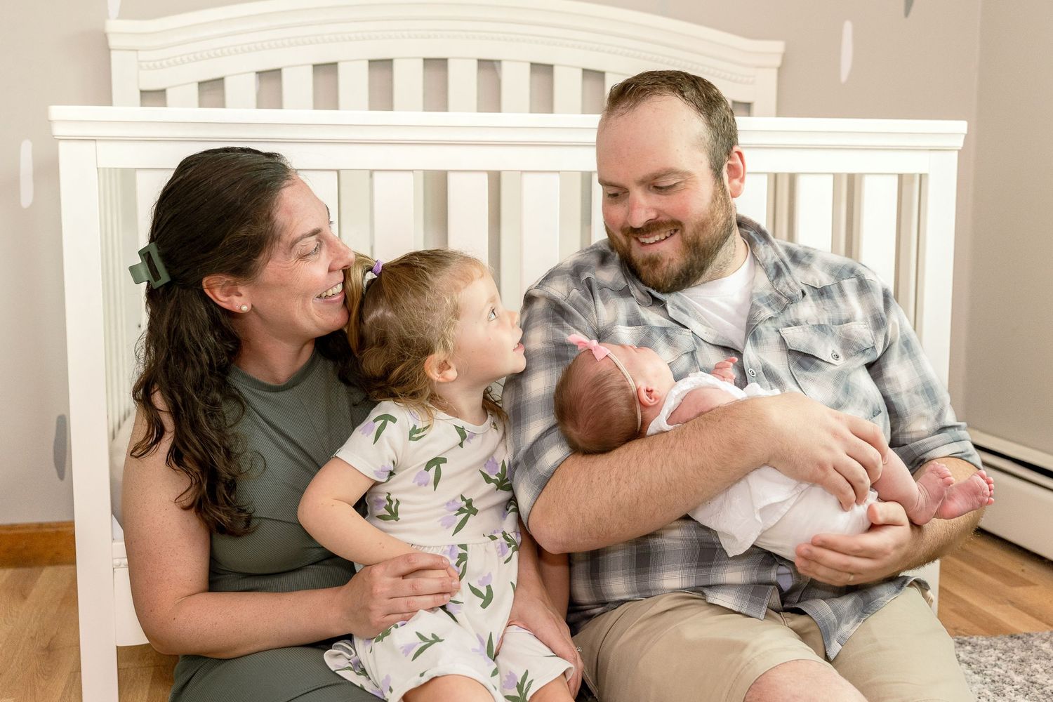 Family gathered around white crib sharing tender moment with newborn.