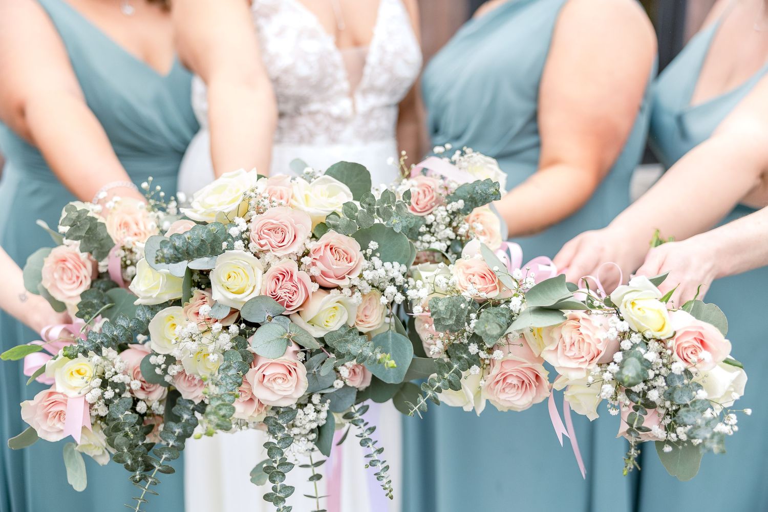 Bridesmaids in blue dresses holding delicate pink and white floral bouquets.