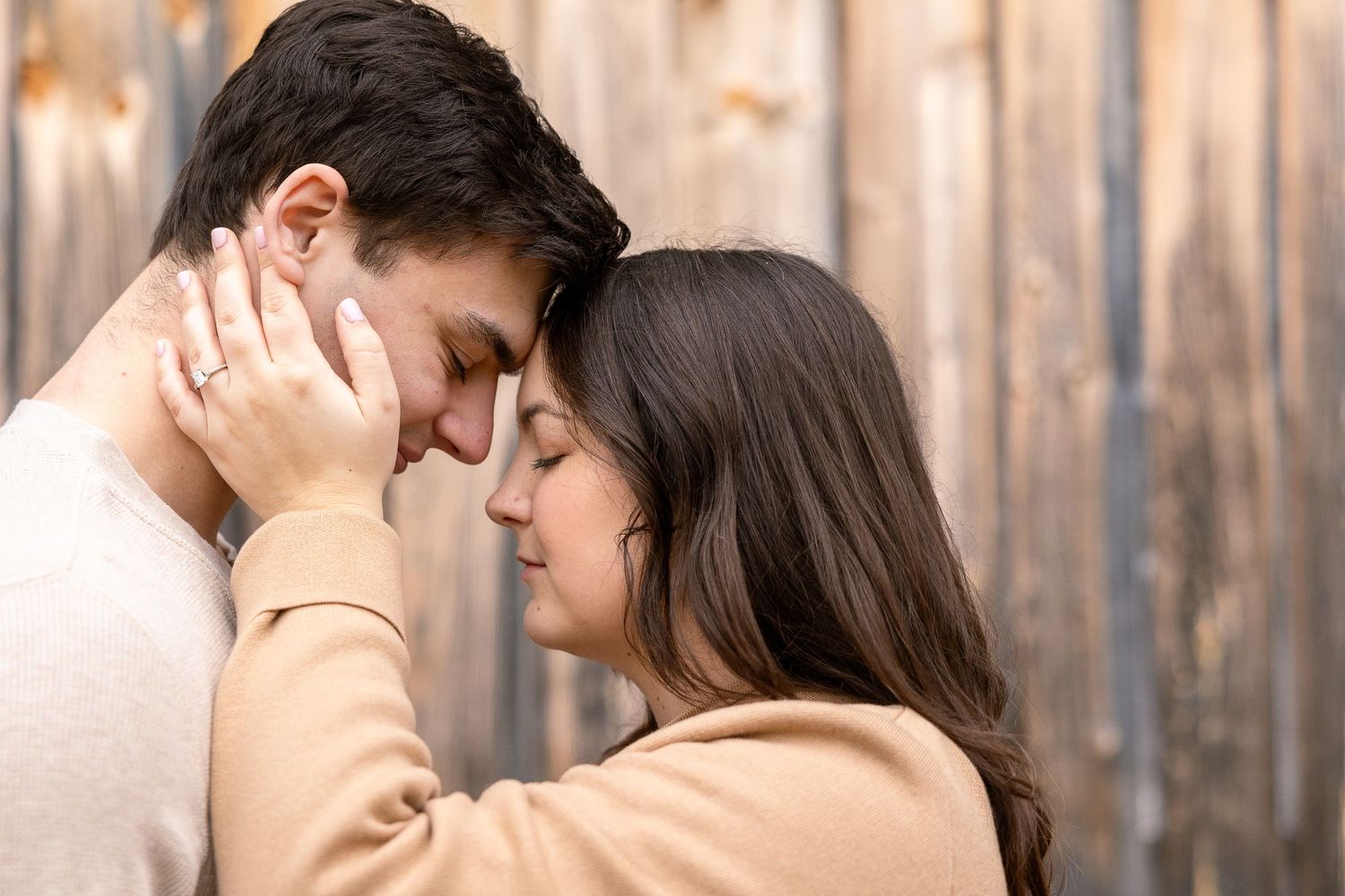 Tender romantic couple sharing an intimate moment while standing close together in front of a wooden fence.