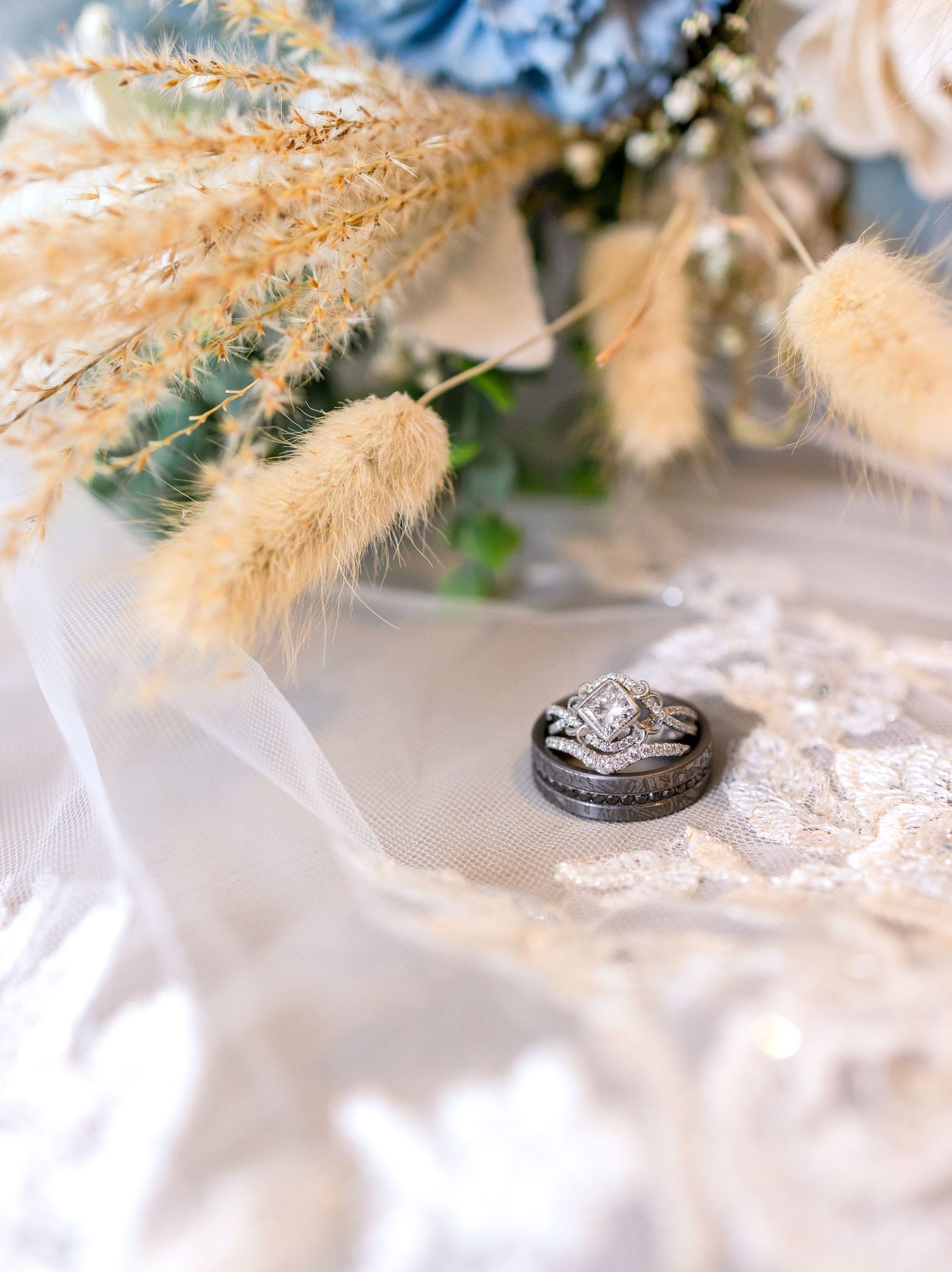 Wedding rings nestled among dried pampas grass and lace fabric.