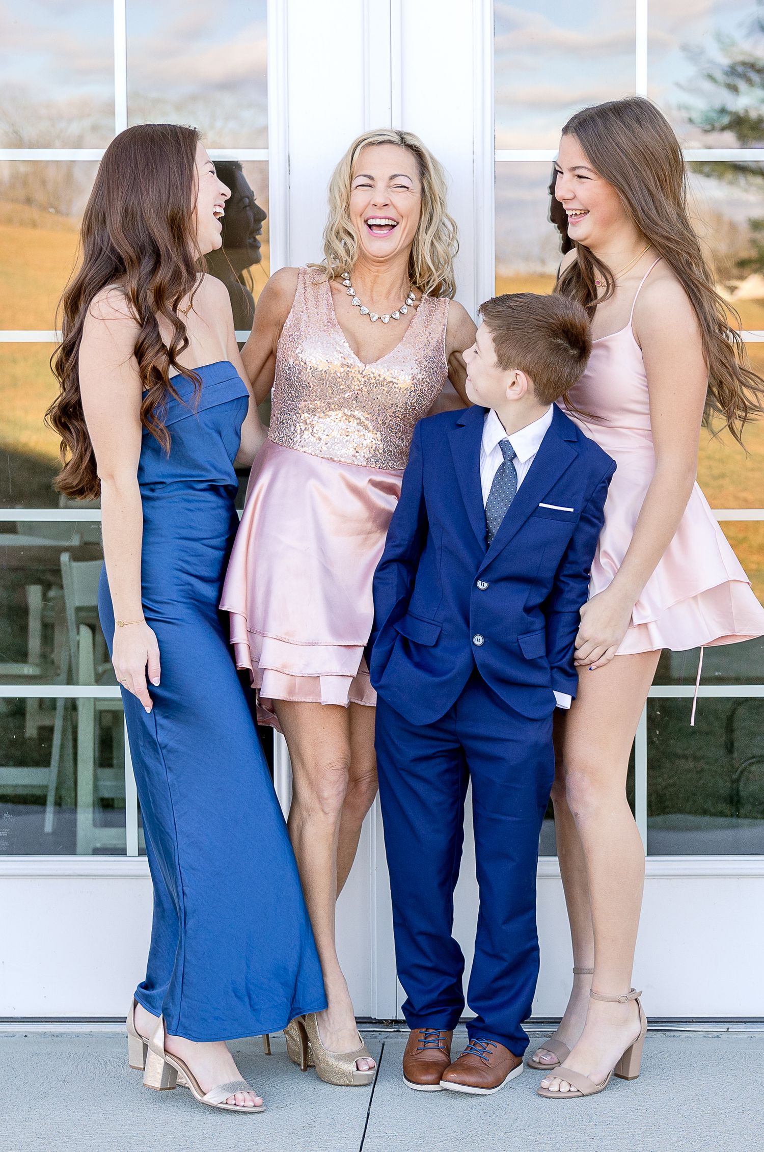 A family group in formal attire shares a candid laughing moment together during a special occasion.
