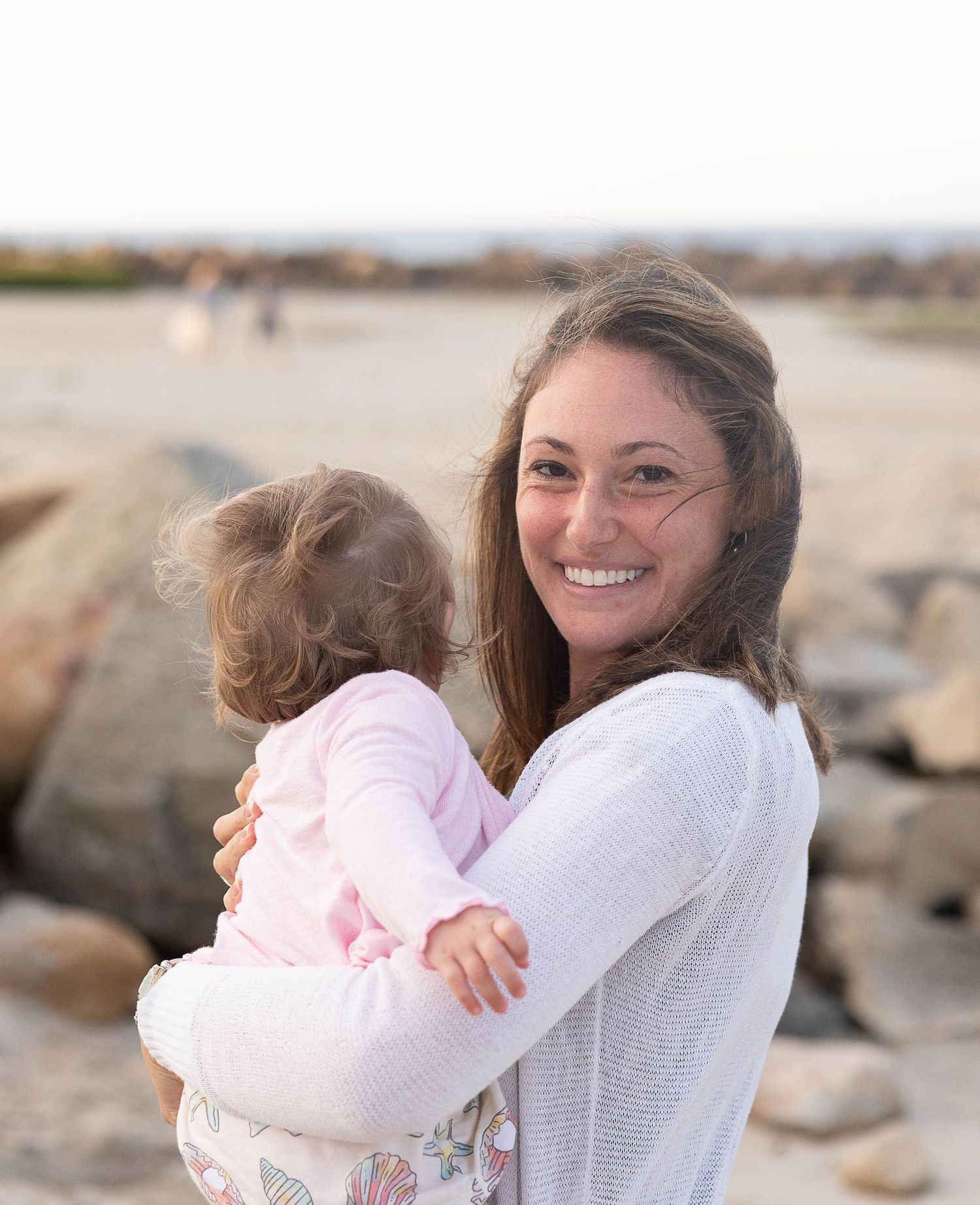 Mother and baby share joyful moment together at rocky beach during sunset.