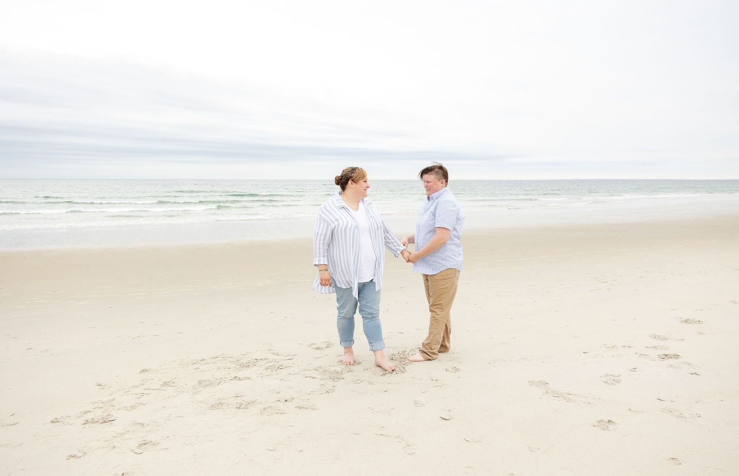 A couple strolls together on a serene beach with an overcast sky.