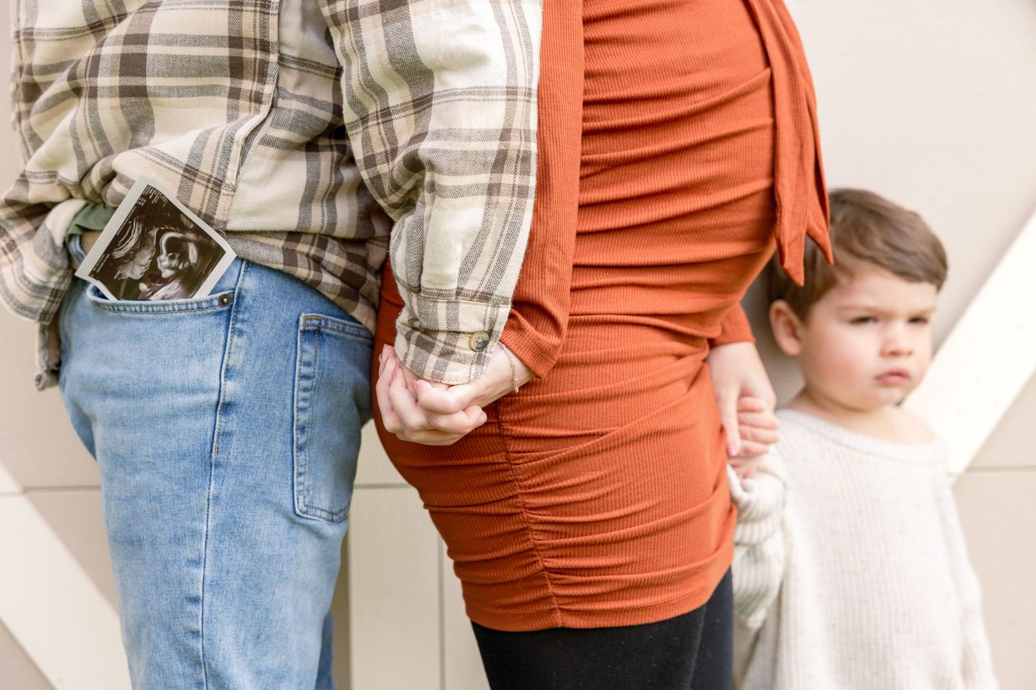 Family members stand together wearing casual clothing including a plaid shirt, ruched orange dress and denim jeans.