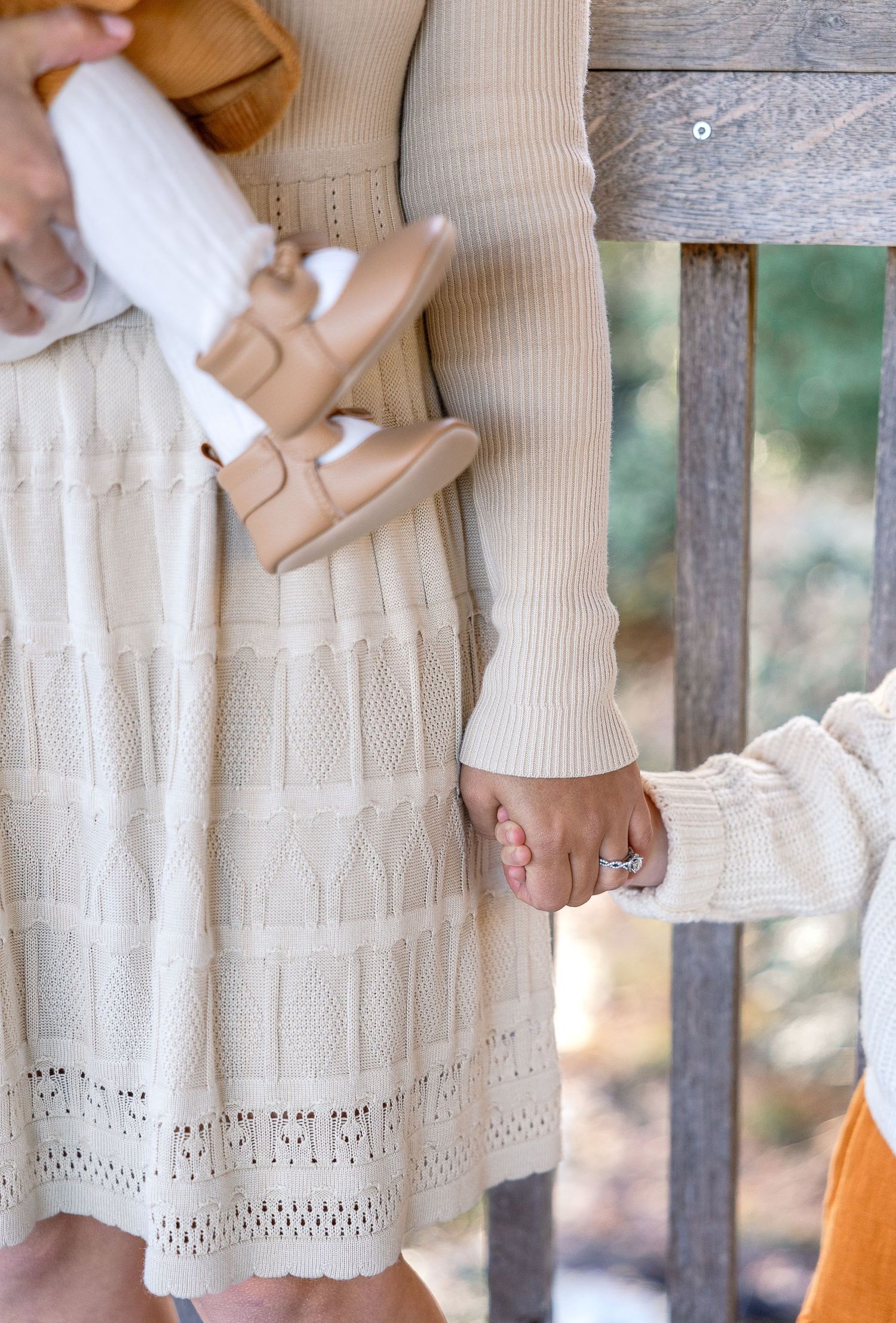 Close-up of someone wearing a cream knit sweater and white lace skirt holding a child's hand.