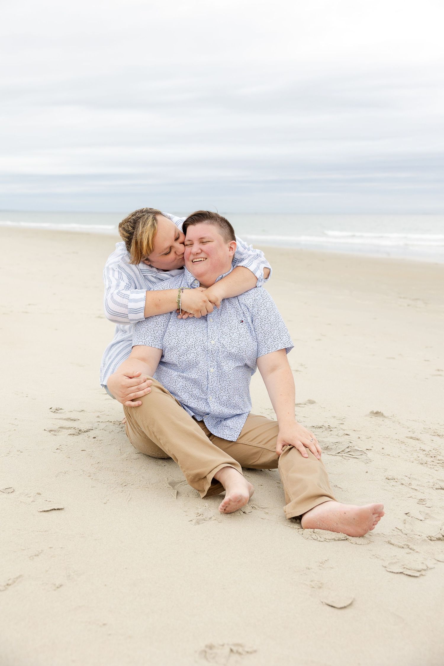 A joyful couple shares a romantic moment together while sitting on a sandy beach by the ocean.