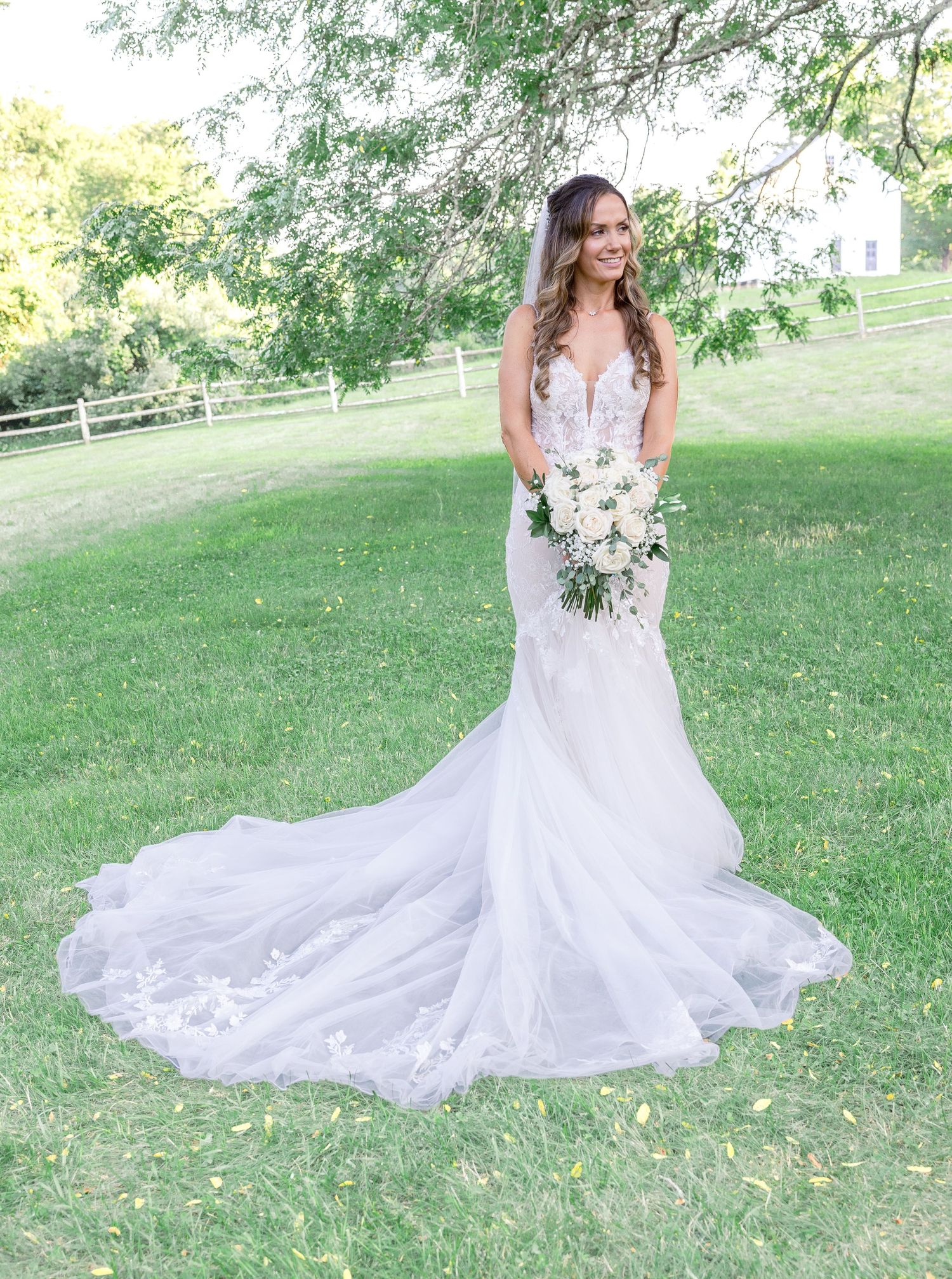 Beautiful white mermaid wedding gown with lace details and flowing train photographed outdoors in a scenic garden setting.