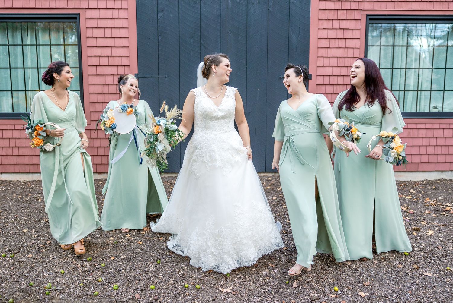 A wedding party wearing mint green bridesmaid dresses and a white wedding gown pose in front of a brick wall.