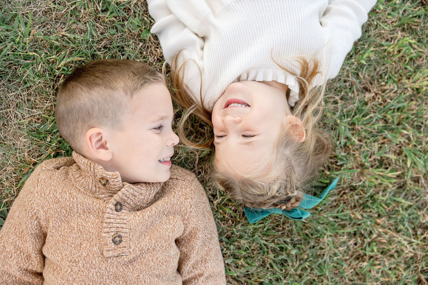 Two people lie on grass looking at each other while wearing cozy fall sweaters.