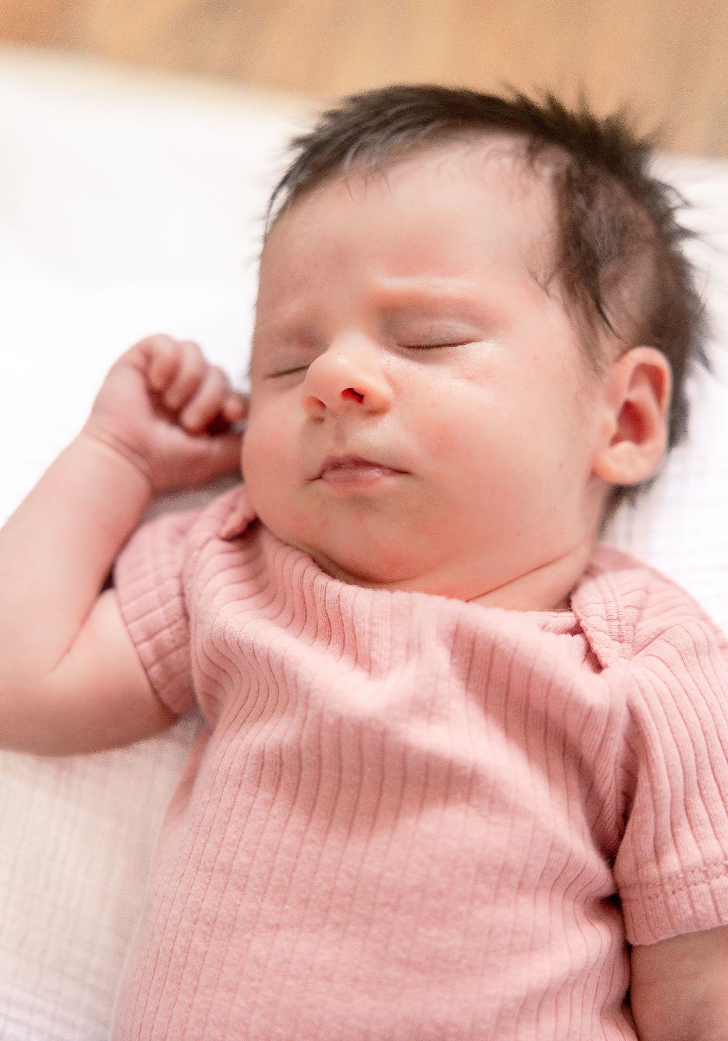 A sleeping baby in a soft pink knit outfit rests peacefully on a light surface.