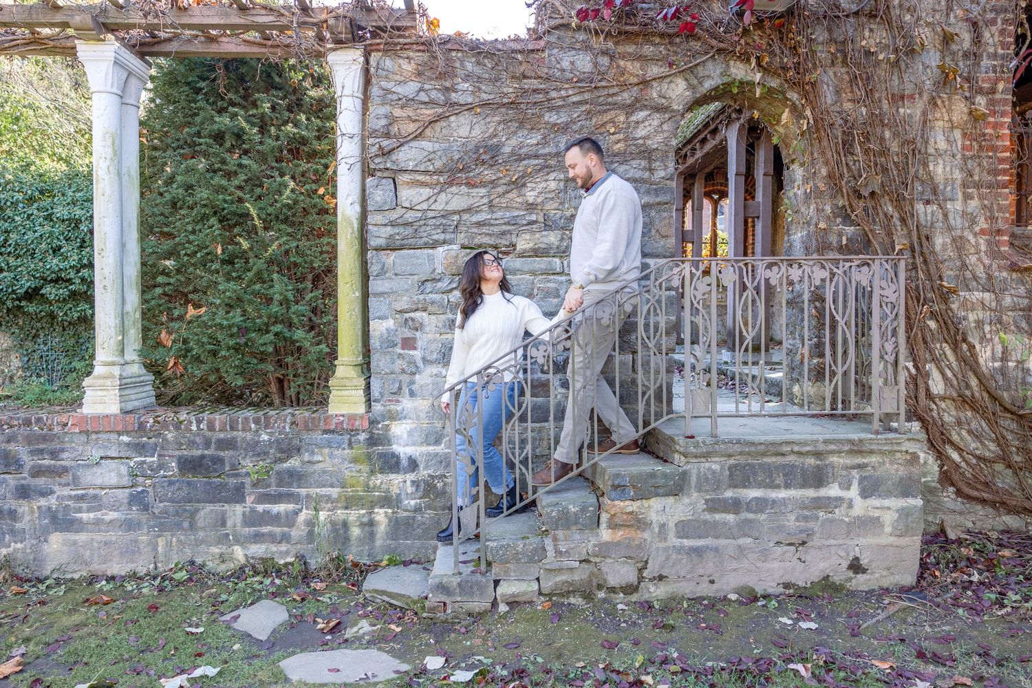 Stone steps lead to an ivy-covered stone archway at a historic mansion with white pillars.