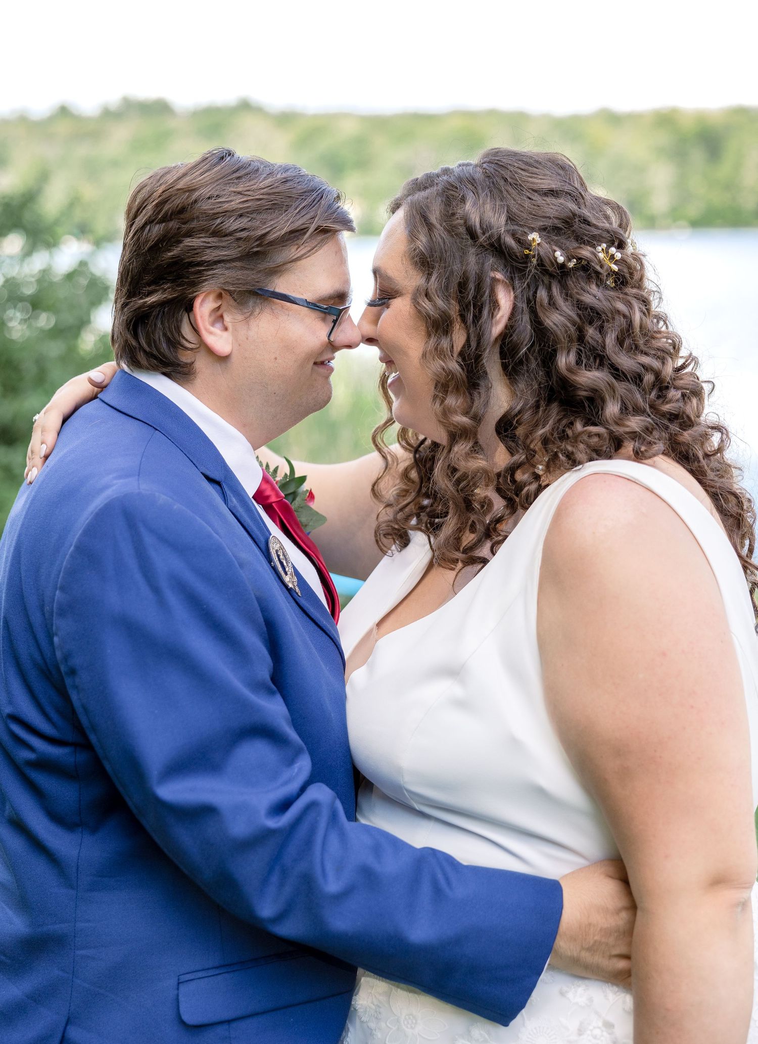A couple in wedding attire share an intimate moment outdoors with a water view in the background.
