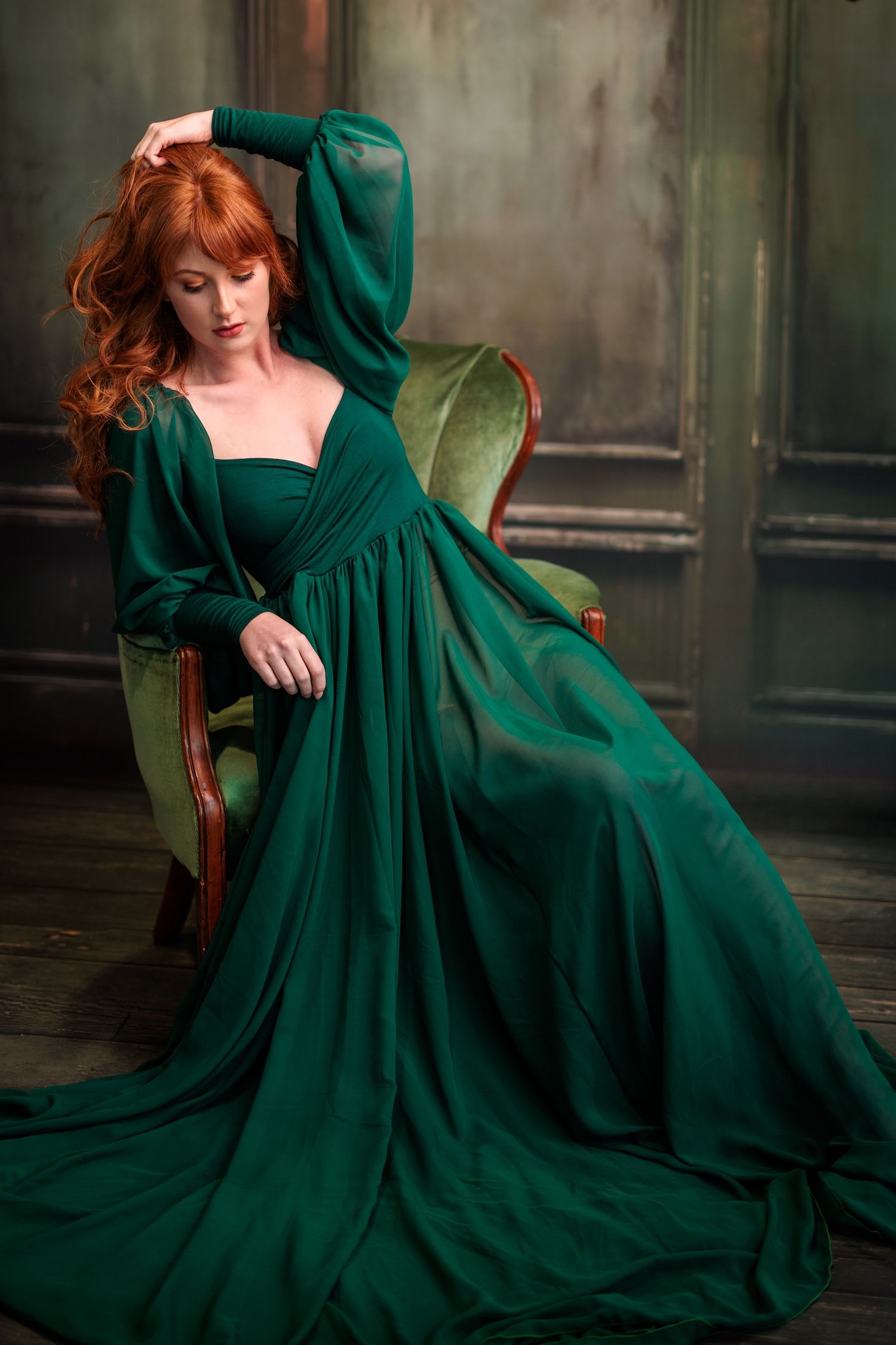 A dramatic emerald green ball gown with puff sleeves drapes elegantly across an antique chair.