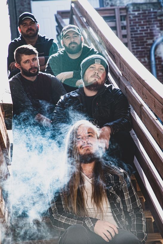 Group sits on outdoor wooden stairs with smoke effects creating dreamy atmosphere in urban setting.