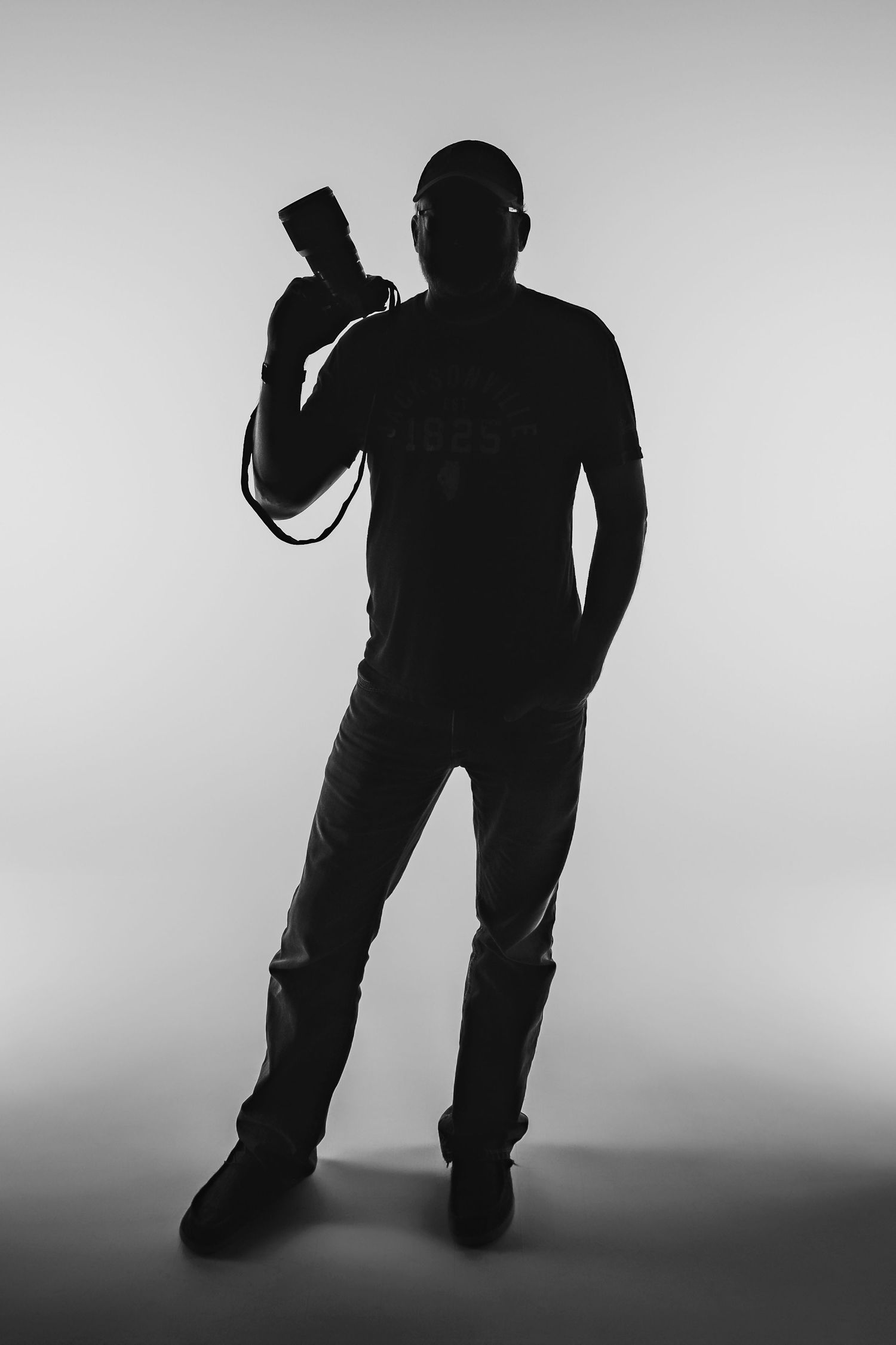 Black and white silhouette of person in casual attire holding camera equipment against light background.