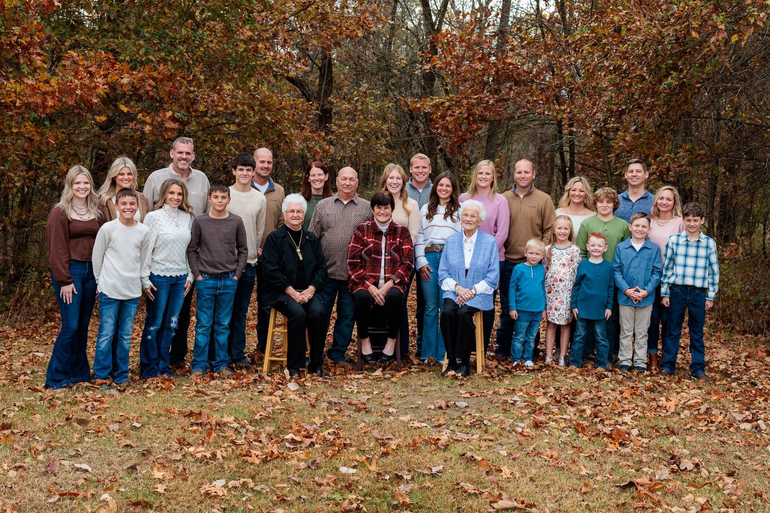 Large family poses together for outdoor autumn portrait surrounded by colorful fall foliage and trees.