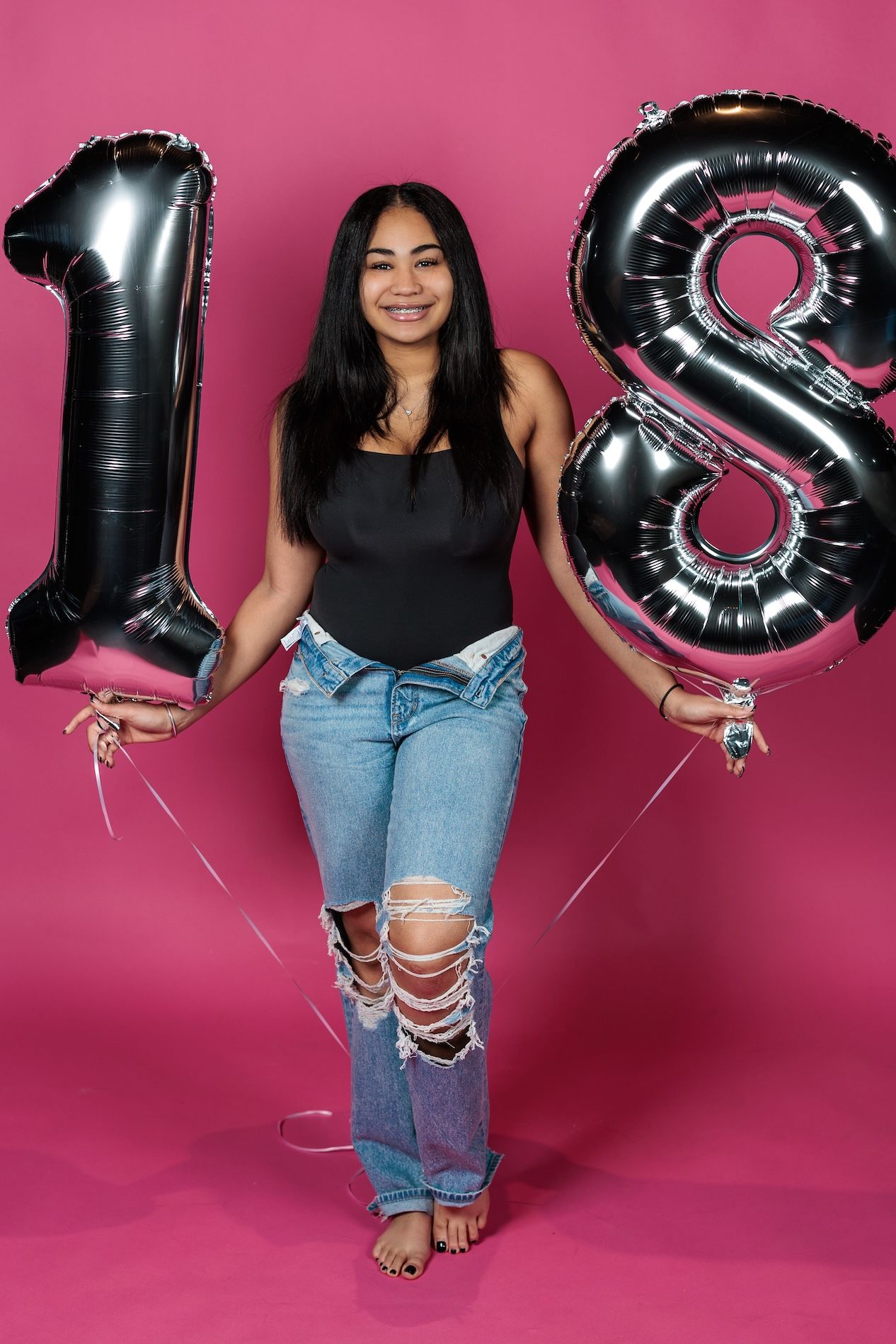 A festive birthday celebration scene with large black metallic number balloons spelling out 18 against a pink backdrop.