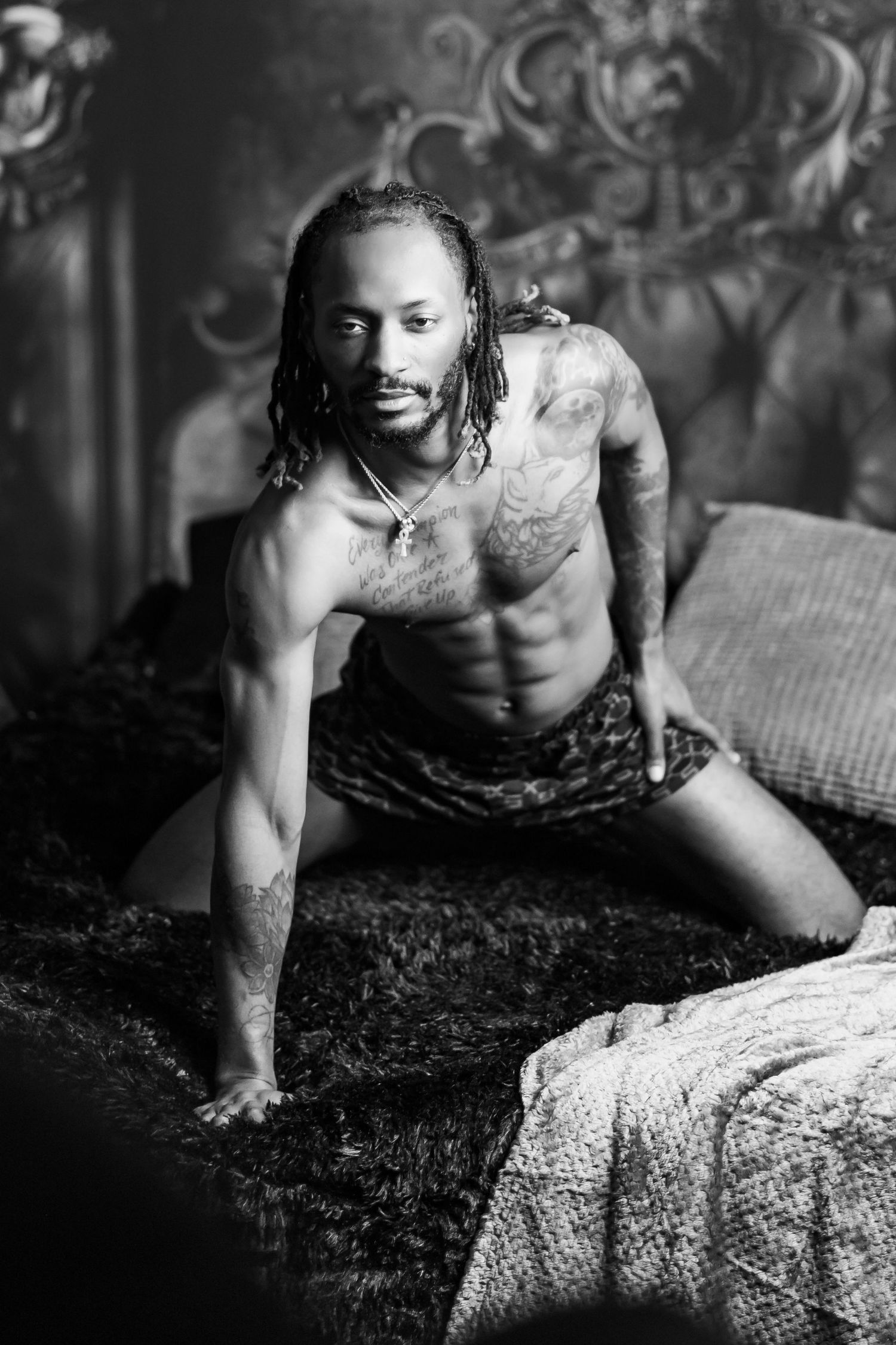 Black and white artistic portrait of a shirtless athletic person with dreadlocks in dramatic lighting.