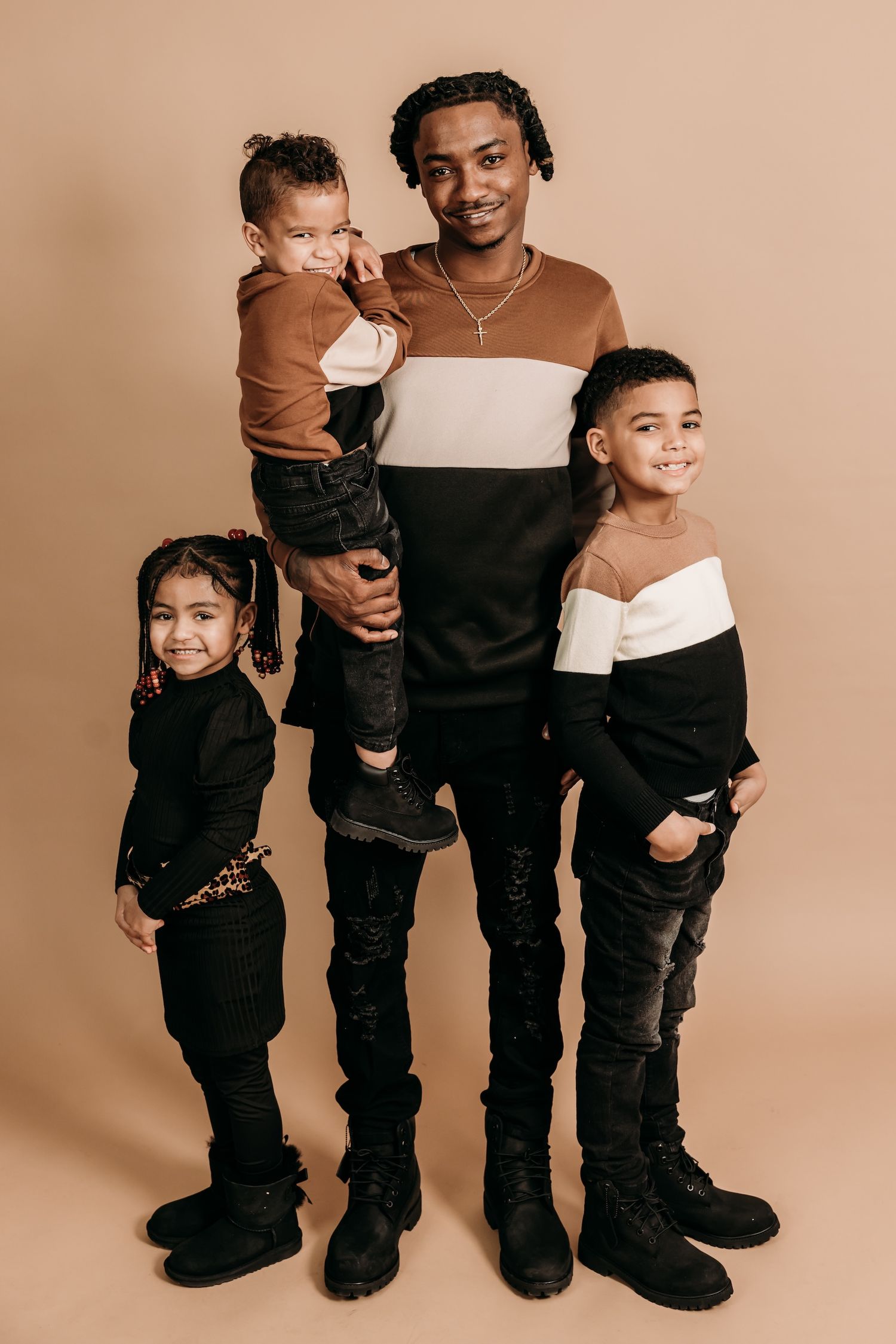 Four people pose in coordinating brown and black striped sweaters and pants against a neutral studio background.