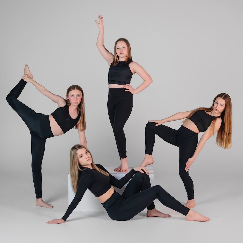 A group poses in black athletic wear while performing flexible dance and yoga poses on a gray background.