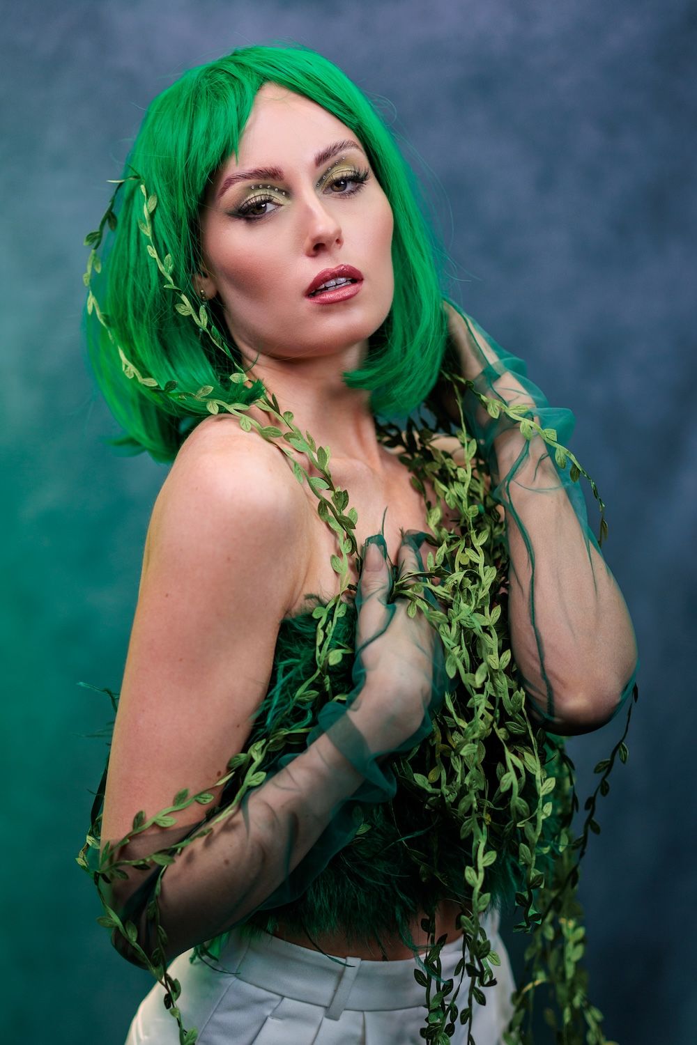 Model with vibrant green hair and sheer sleeves poses in a mythical forest-inspired photoshoot with climbing vines.