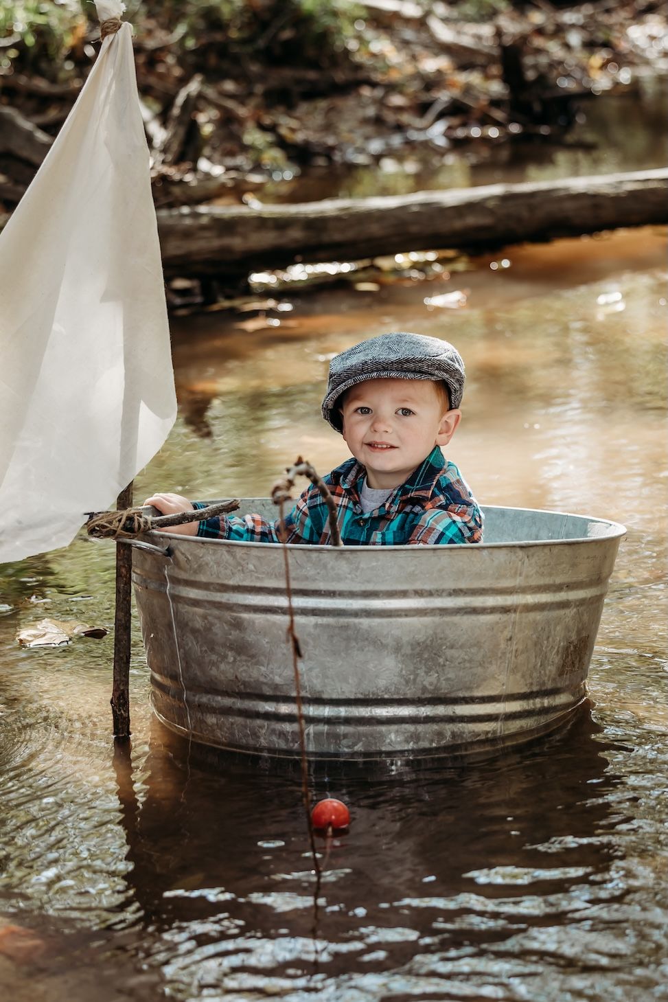 A rustic bathtub boat with a white sail sits in a shallow stream while creating an imaginative adventure scene.