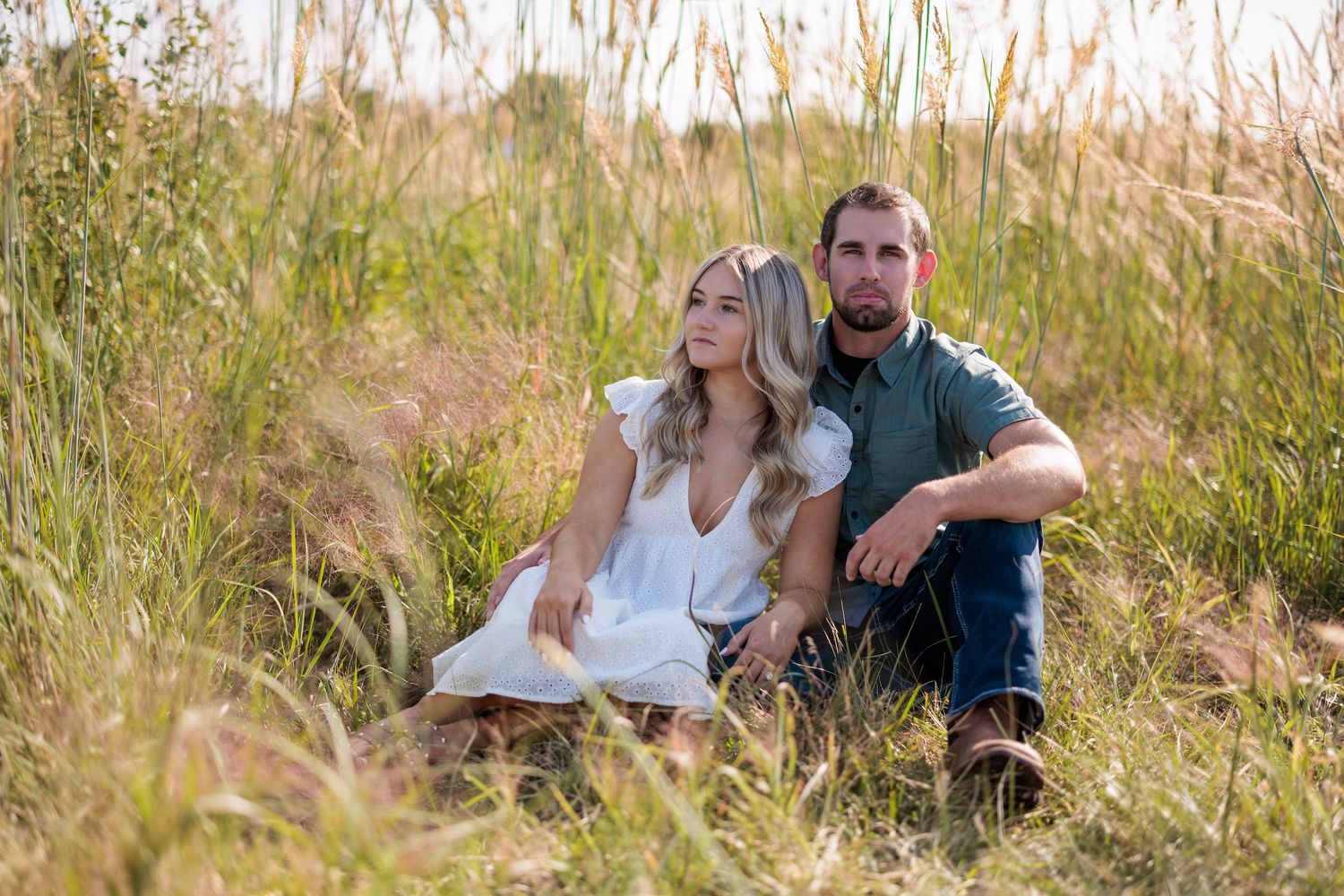 A couple sits together in a serene meadow of tall grass during golden hour.