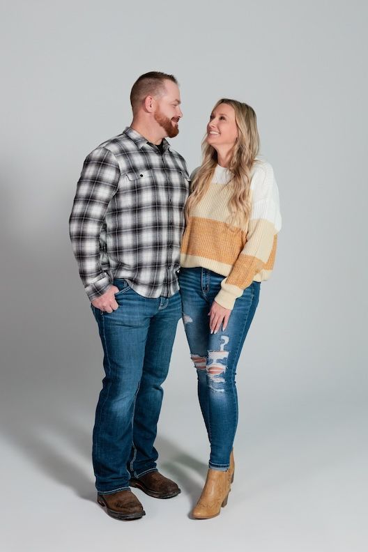 A couple in casual attire laughing together against a gray studio backdrop.